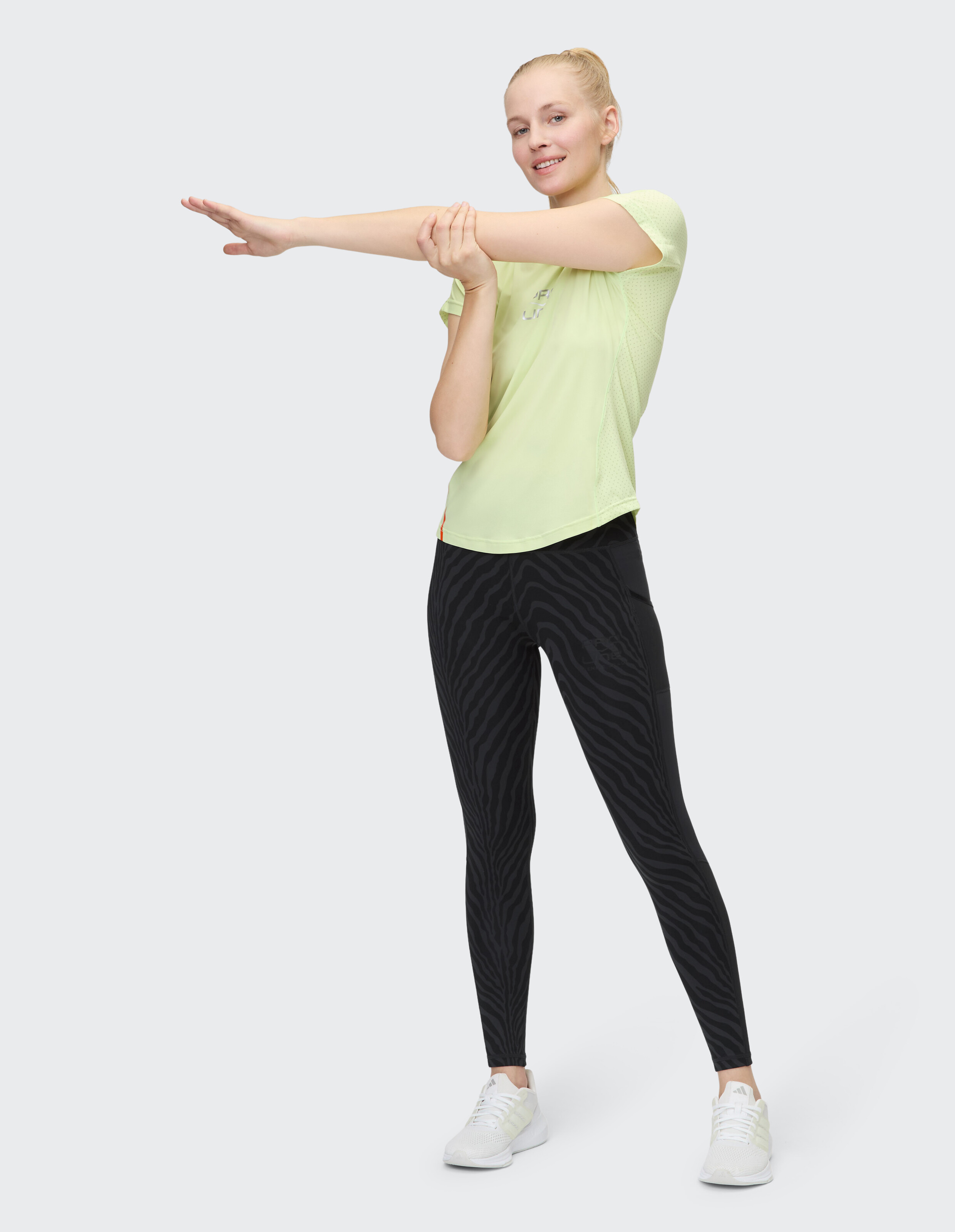 Frau in hellgrünem Sporttop und schwarzen Leggings mit Zebramuster beim Stretching.