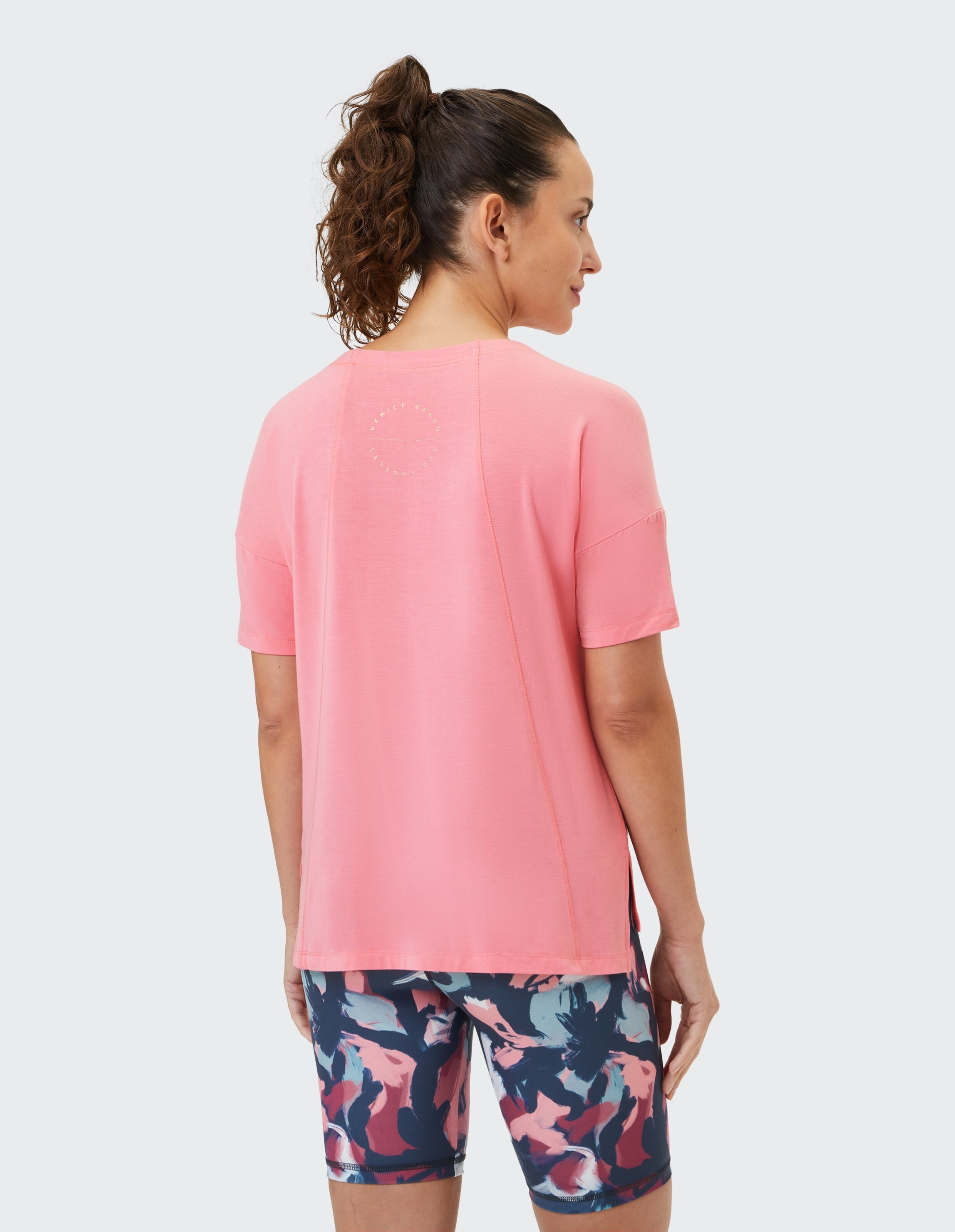 Frau trägt ein rosa Kurzarmhemd von Venice Beach Rae und gemusterte Leggings.