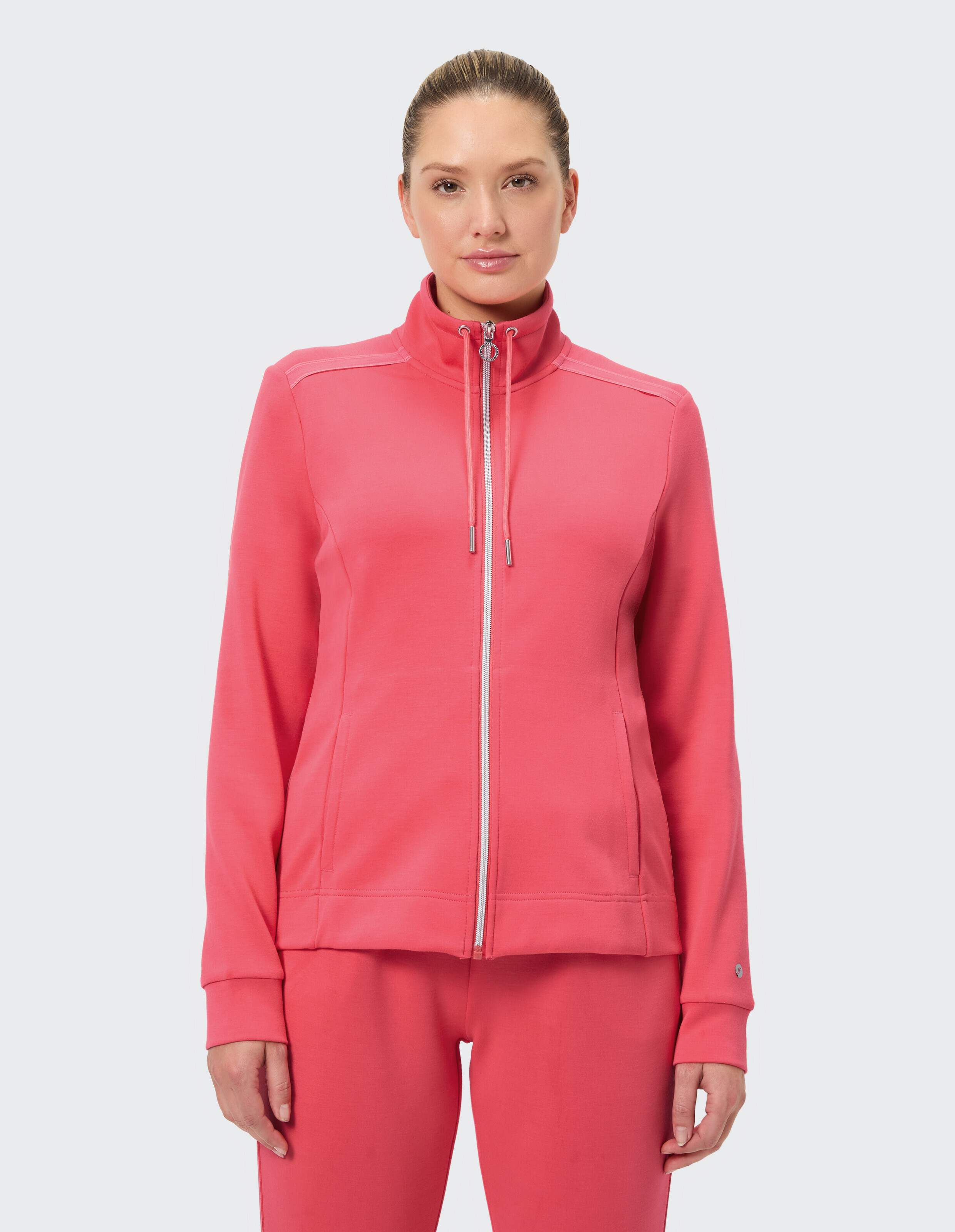 Frau trägt eine rosa Jacke mit Reißverschluss und hohem Kragen, perfekt für Freizeitkleidung oder zum Faulenzen.