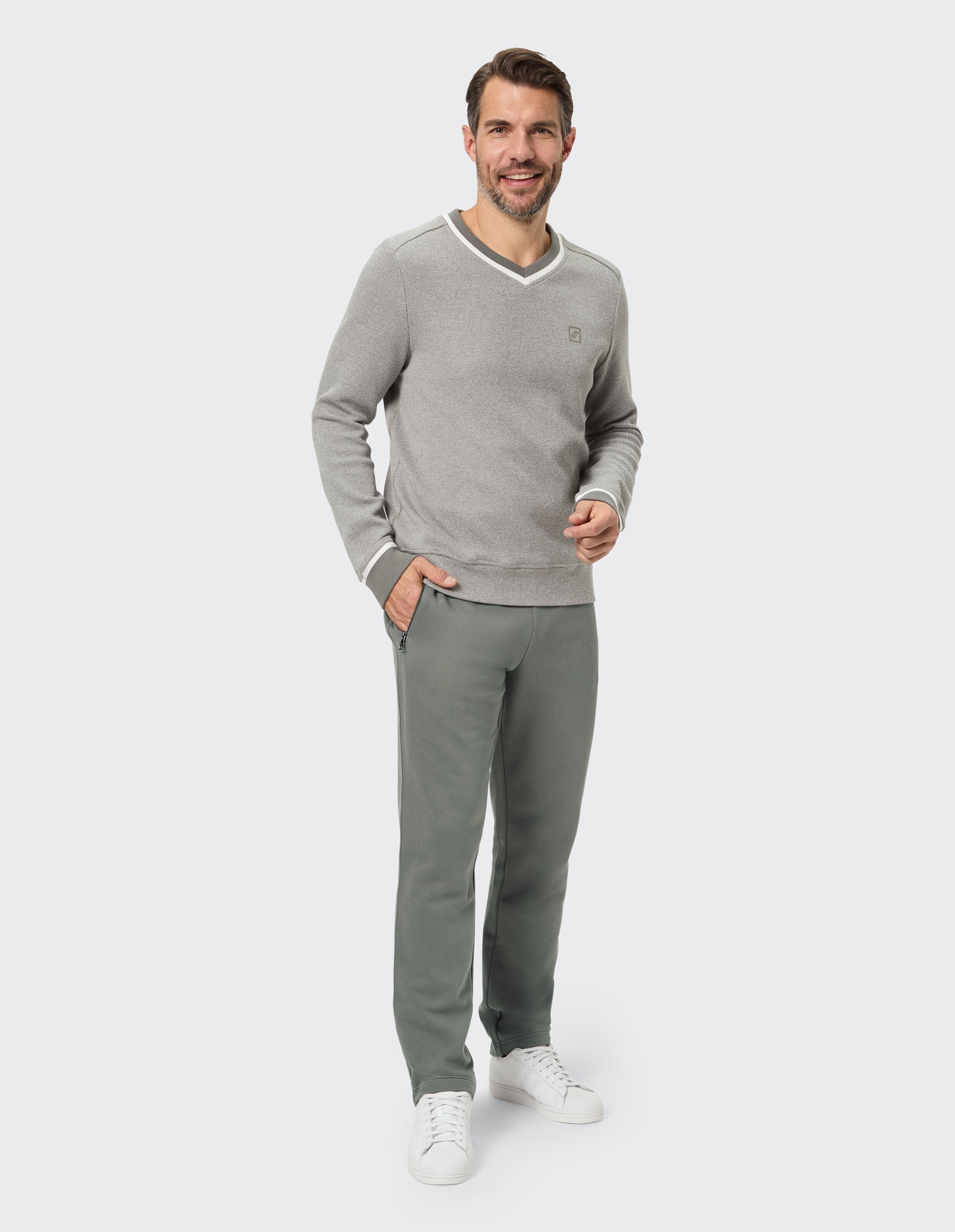 Mann trägt einen grauen Pullover mit V-Ausschnitt und eine olivgrüne Jogginghose für einen gemütlichen, lässigen Look.