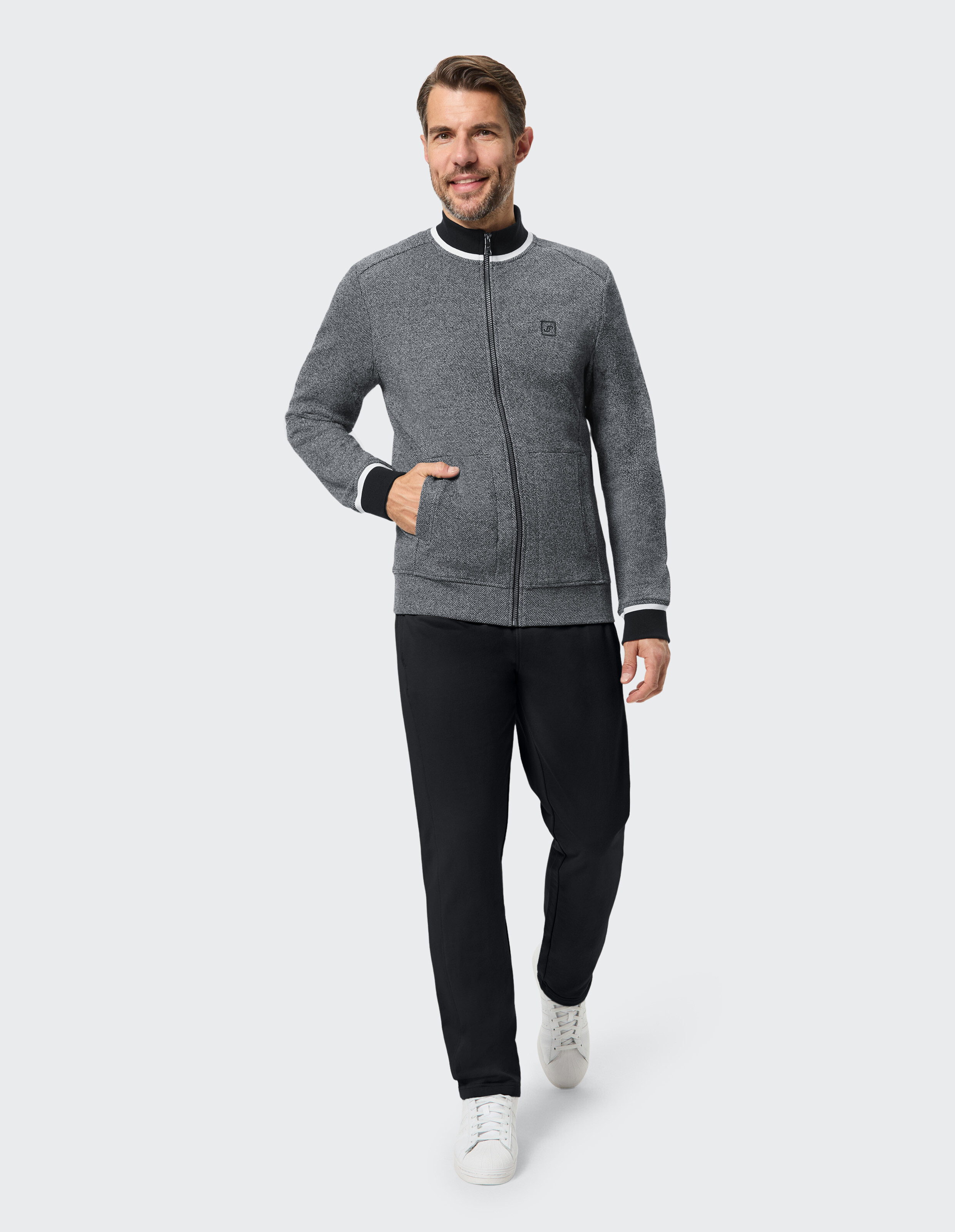 Ein Mann trägt eine graue Jacke mit durchgehendem Reißverschluss und schwarzer Hose.