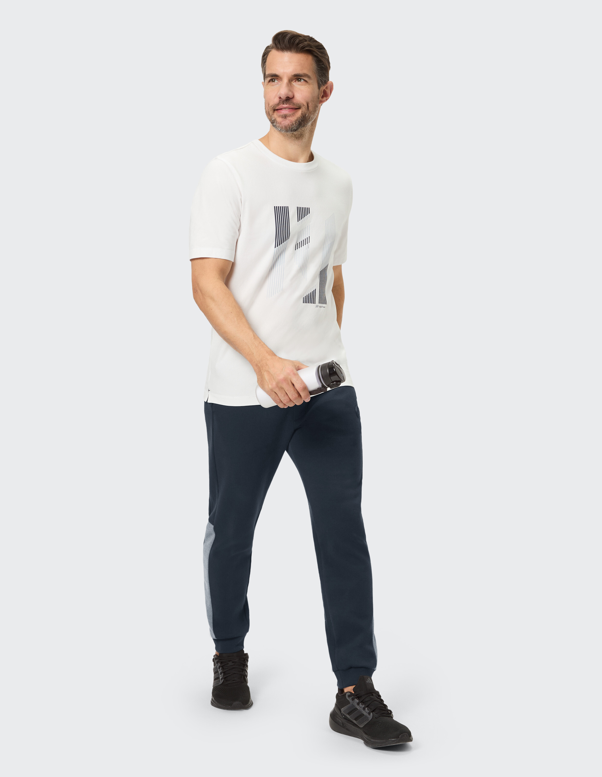 Mann in einem weißen grafischen T-Shirt und dunkelblauen Jogginghosen, stilvolle Freizeitkleidung.