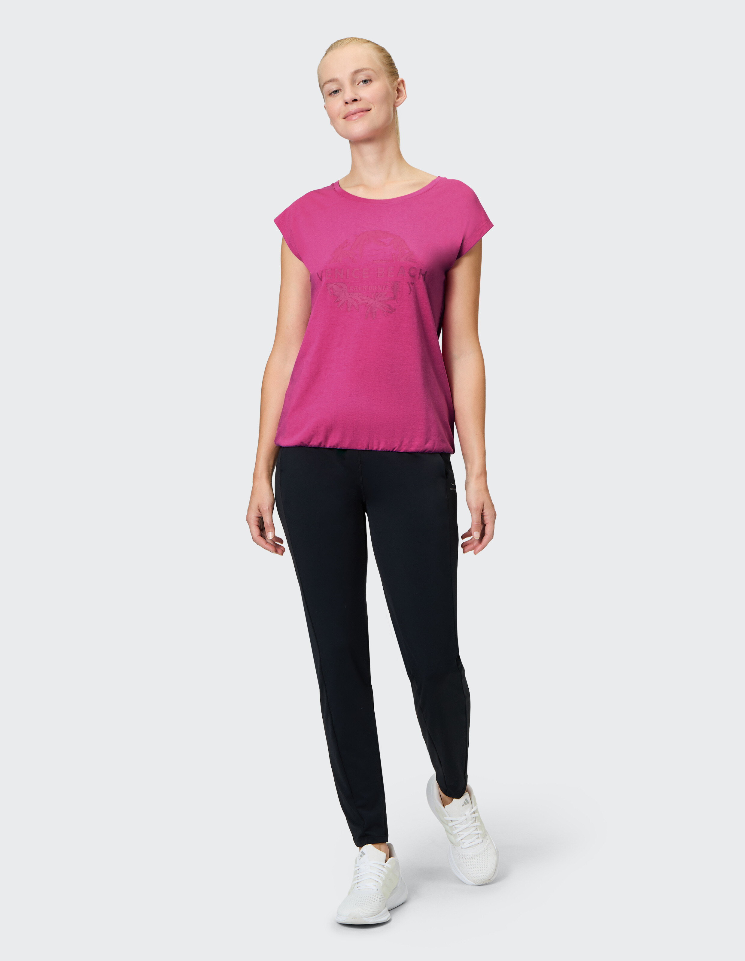 Frau in einem rosa Grafik-T-Shirt und schwarzen Leggings, gestylt für lässigen Komfort.