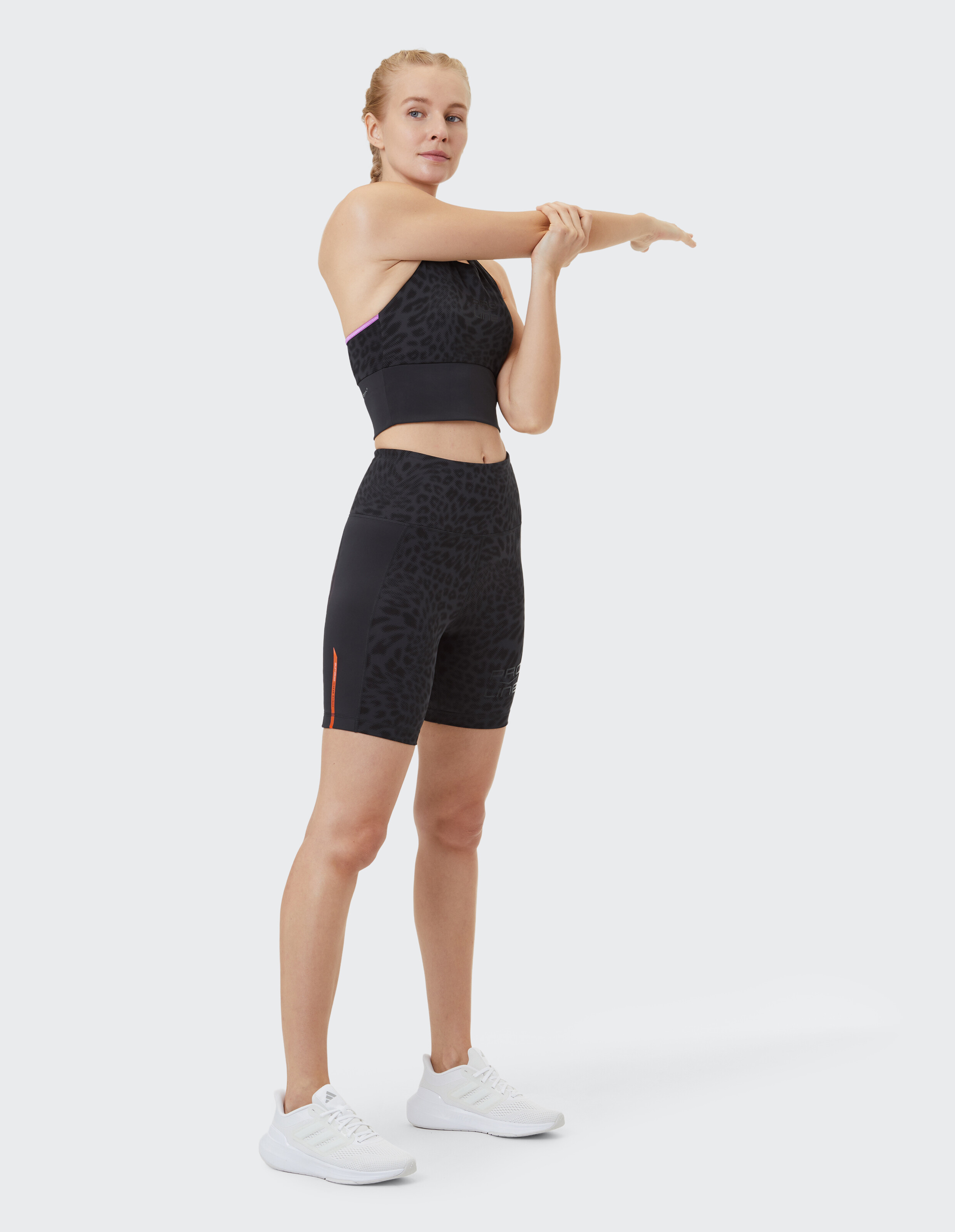 Frau trägt schwarzen Sport-BH mit Leopardenmuster und Bikershorts beim Dehnen.