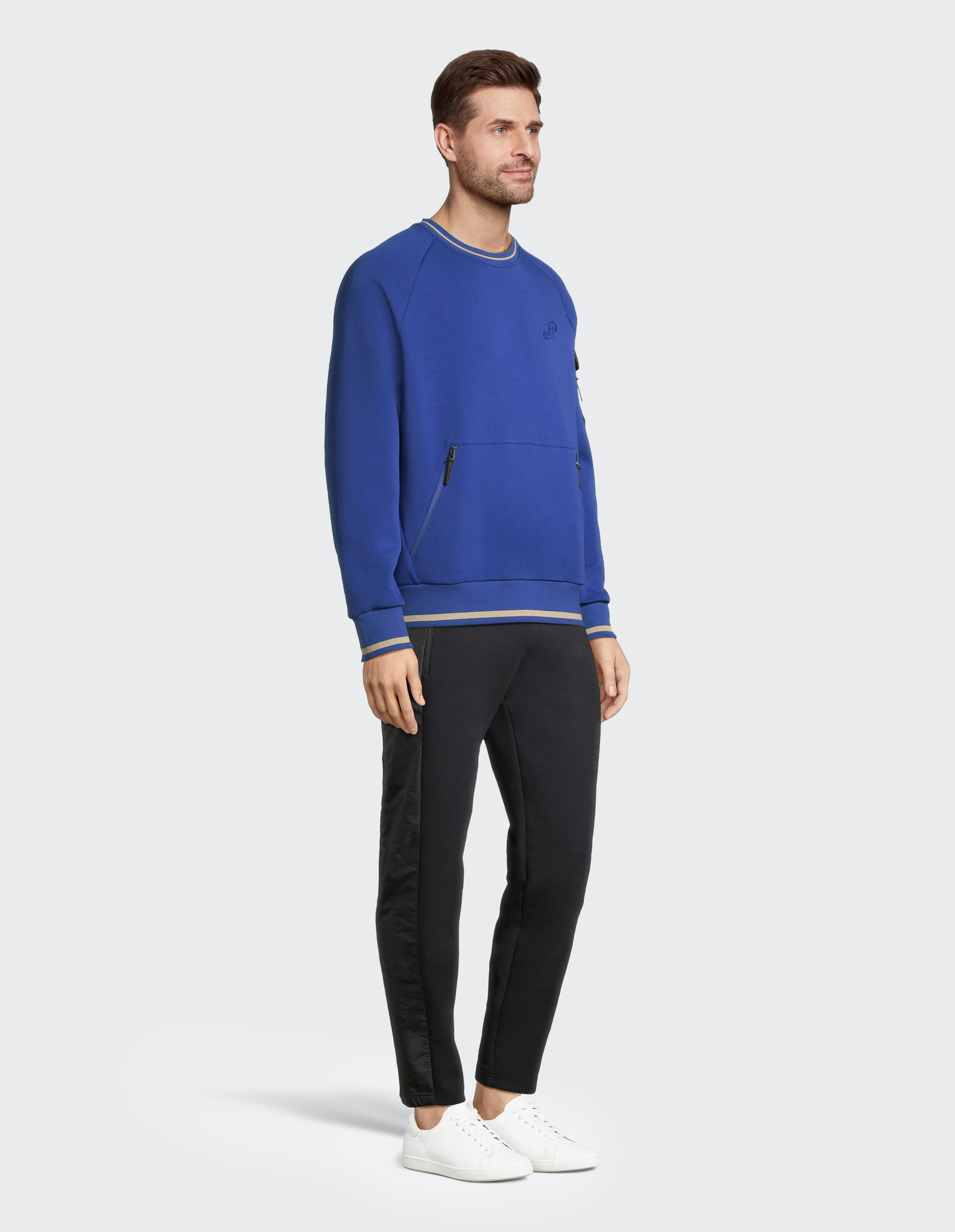 Ein Mann in einem blauen Pullover und schwarzen Jogginghosen steht lächelnd