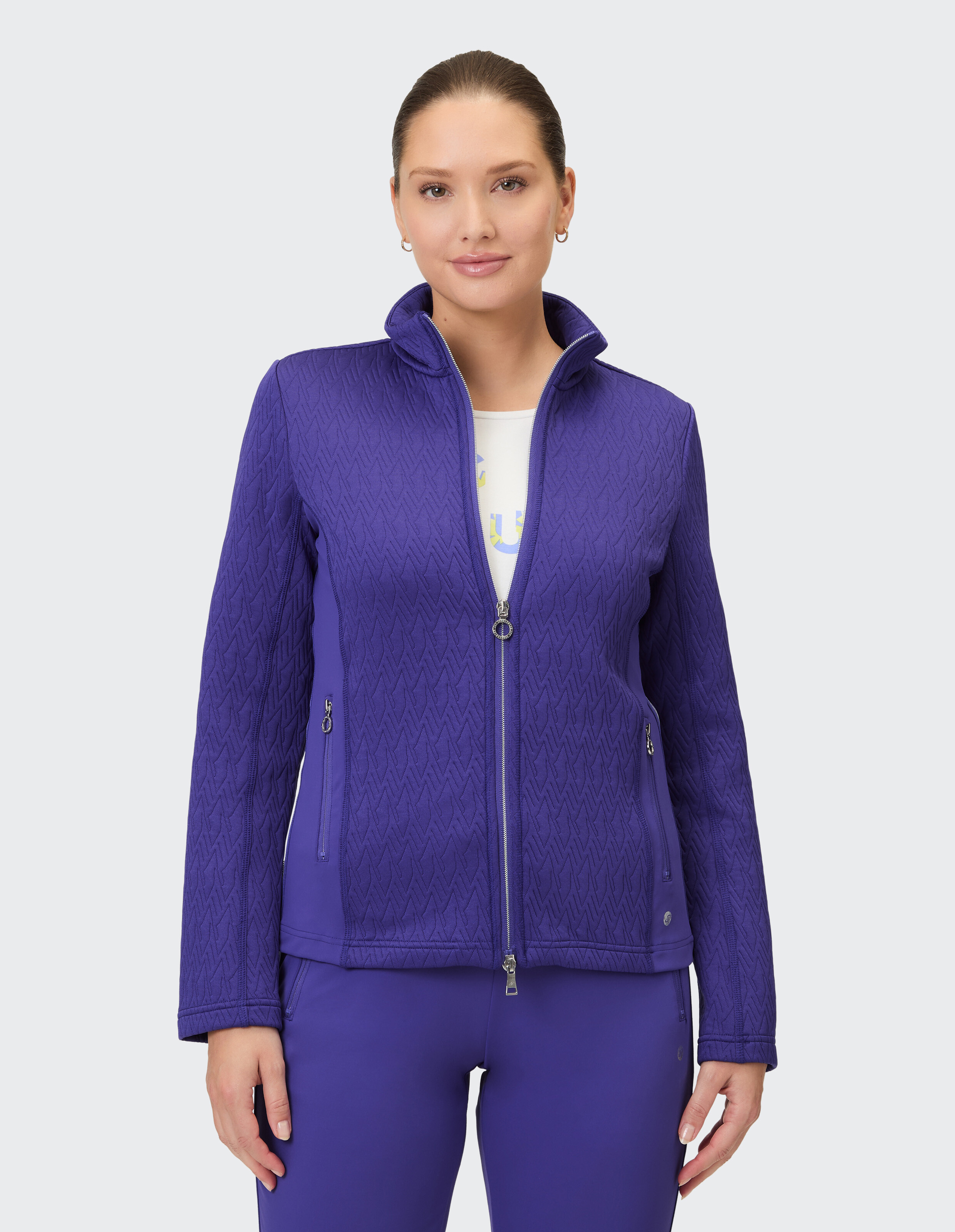 Eine Frau trägt eine schicke, lilafarbene Strickjacke mit Reißverschluss und einem auffälligen Rautenmuster.
