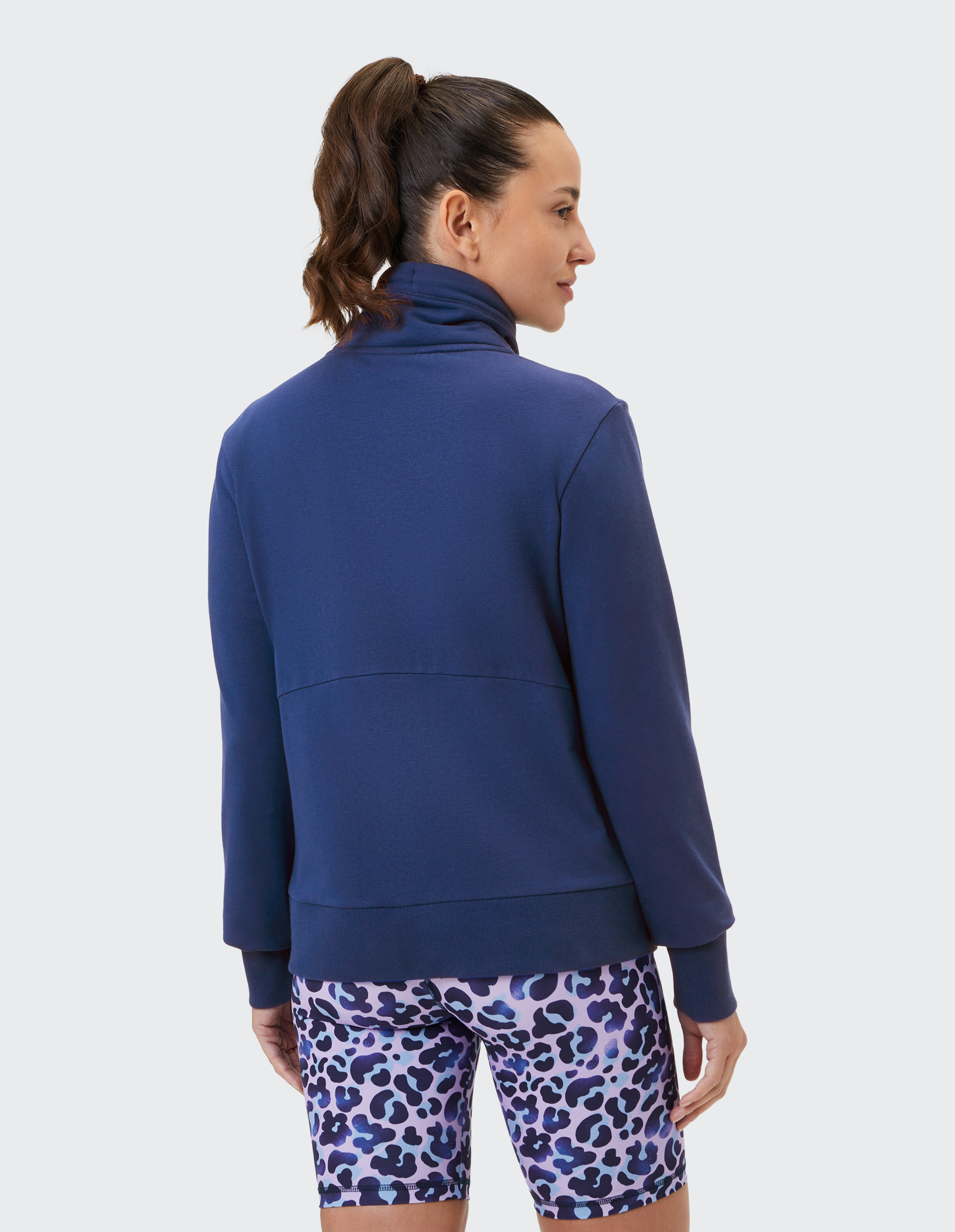 Frau trägt ein dunkelblaues, hochgeschlossenes Sweatshirt und gemusterte Shorts mit Leopardenmuster.