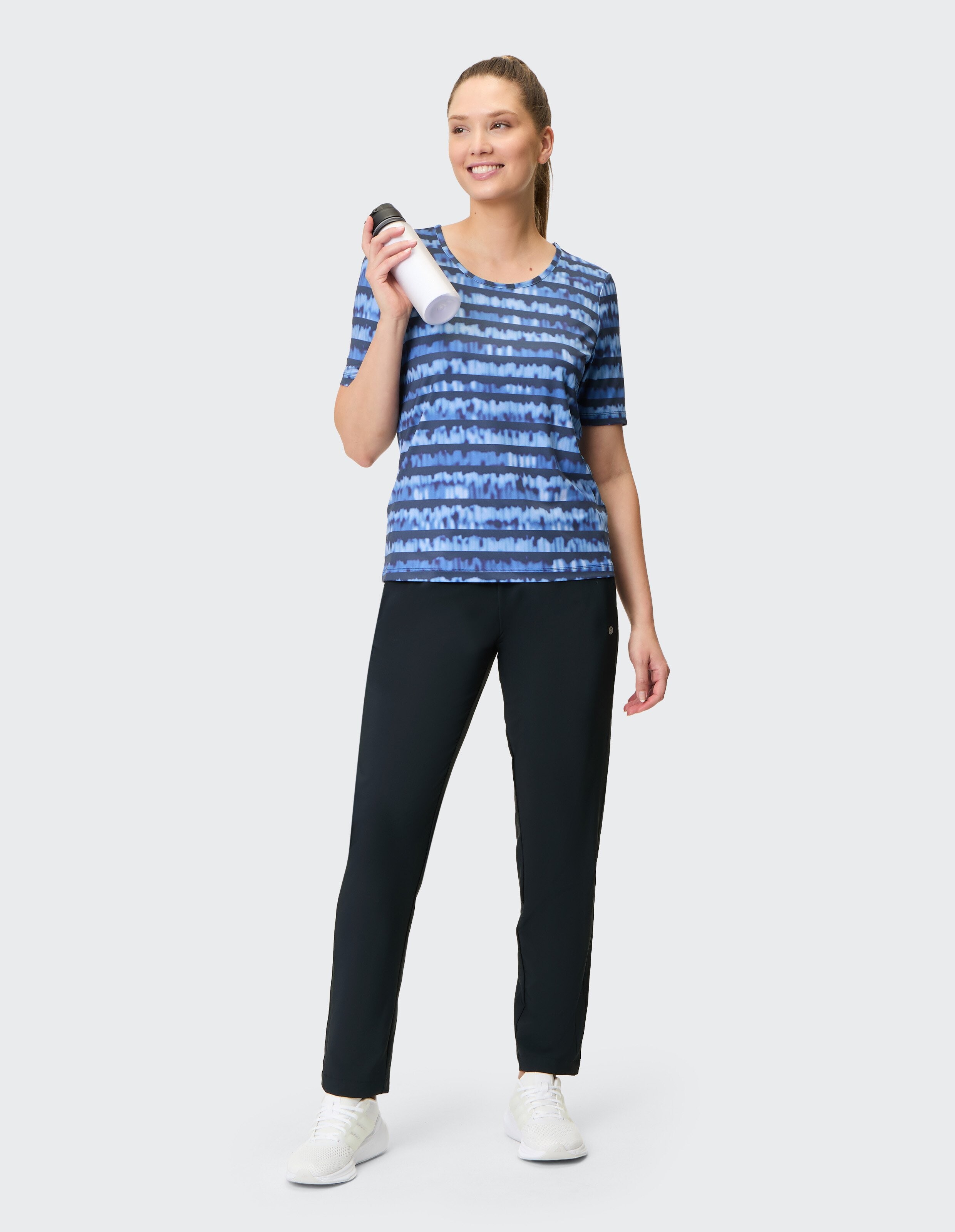 Frau in blau gestreiftem T-Shirt und schwarzer Hose hält eine Wasserflasche in der Hand.