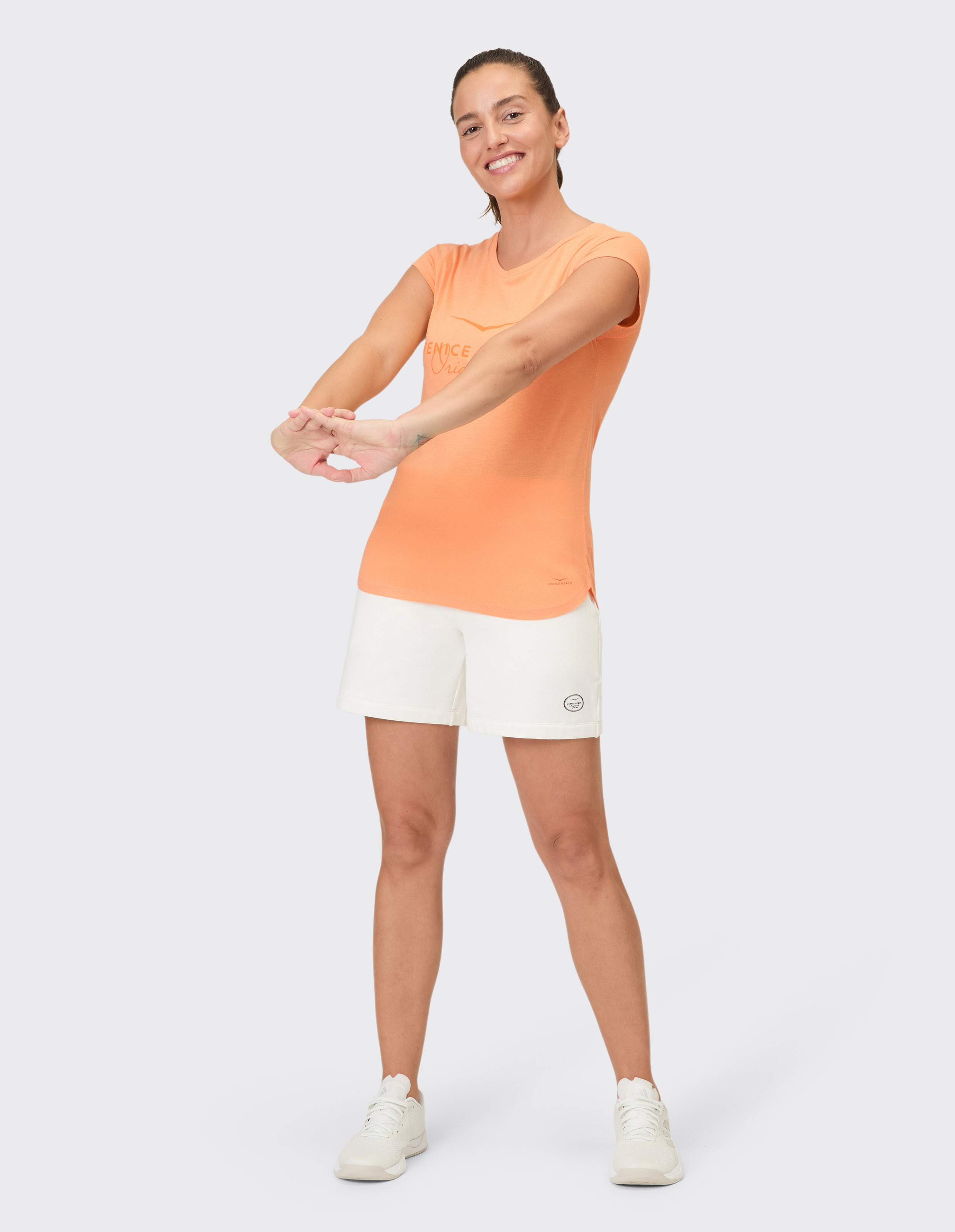 Frau trägt ein orangefarbenes Venice Beach Alisja-T-Shirt und weiße Shorts für Freizeitkleidung.