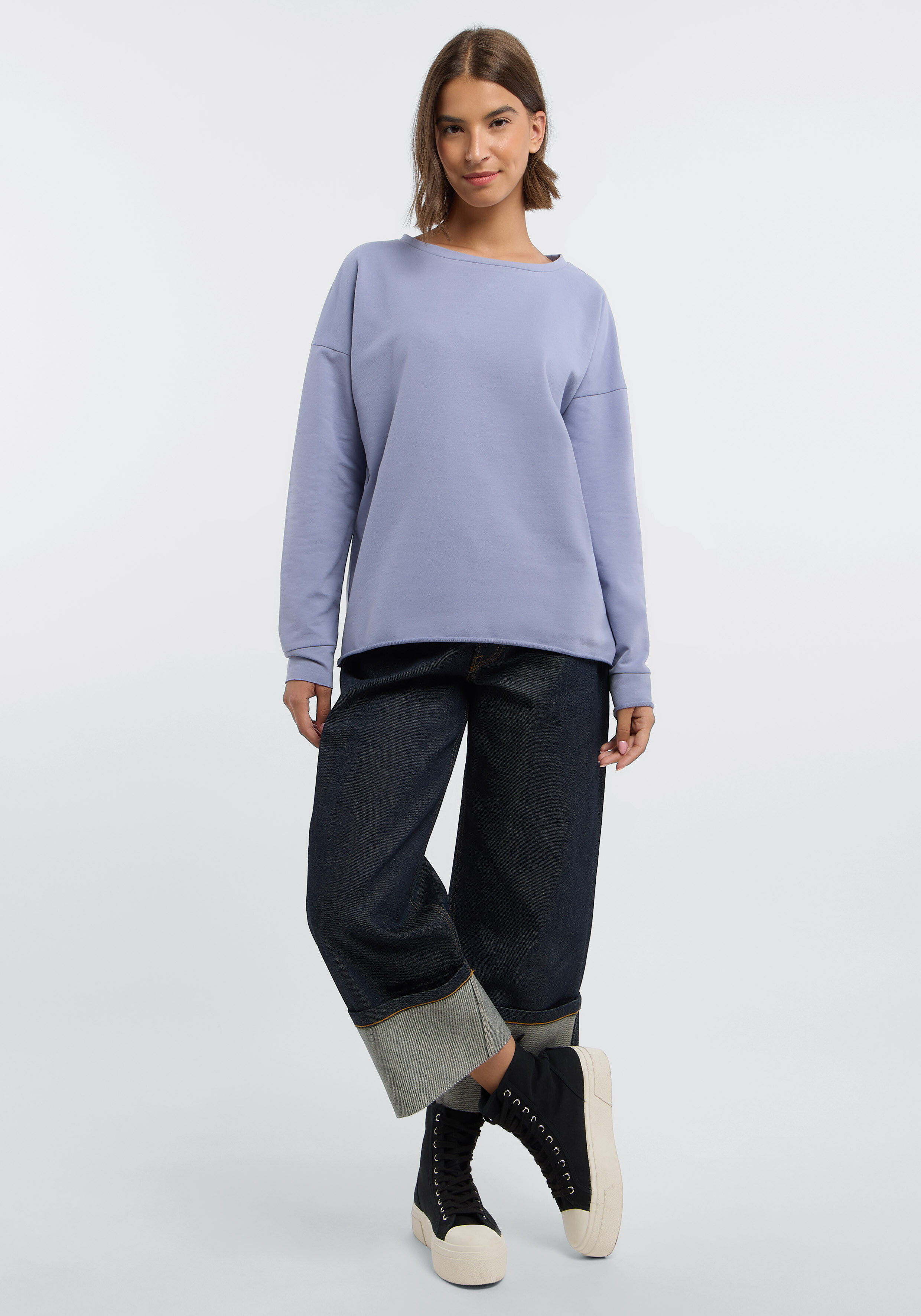 Frau trägt ein kuscheliges hellblaues Sweatshirt und Jeans mit weitem Bein und Bündchen für einen lässigen Stil.