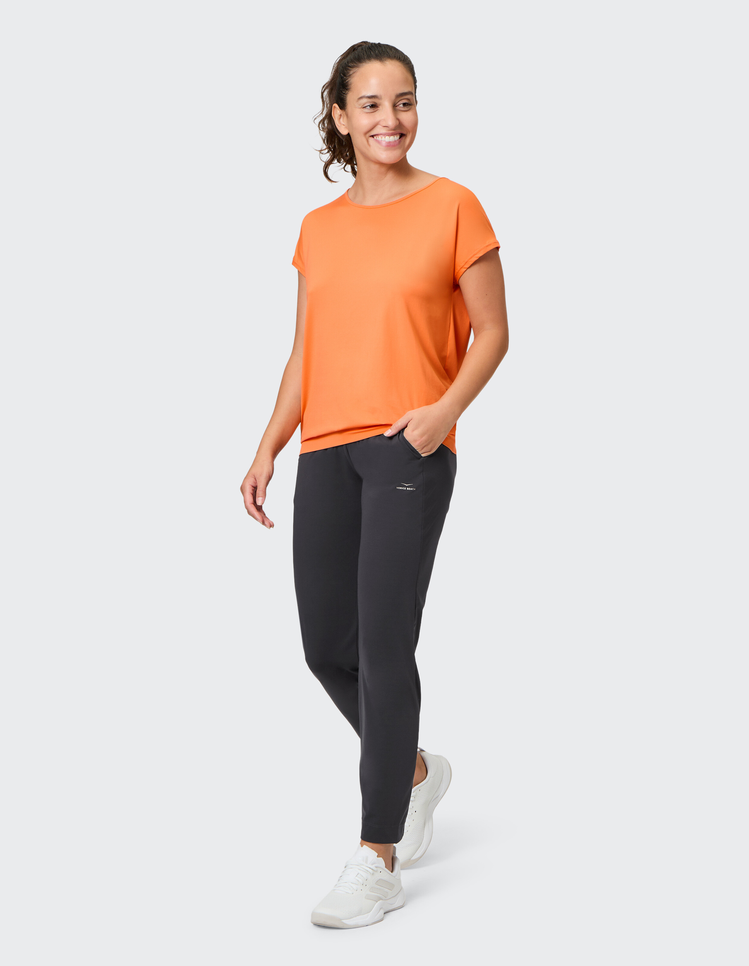 Frau trägt ein gemütliches orangefarbenes T-Shirt und dunkelgraue Freizeit-Jogginghosen für einen entspannten Look.