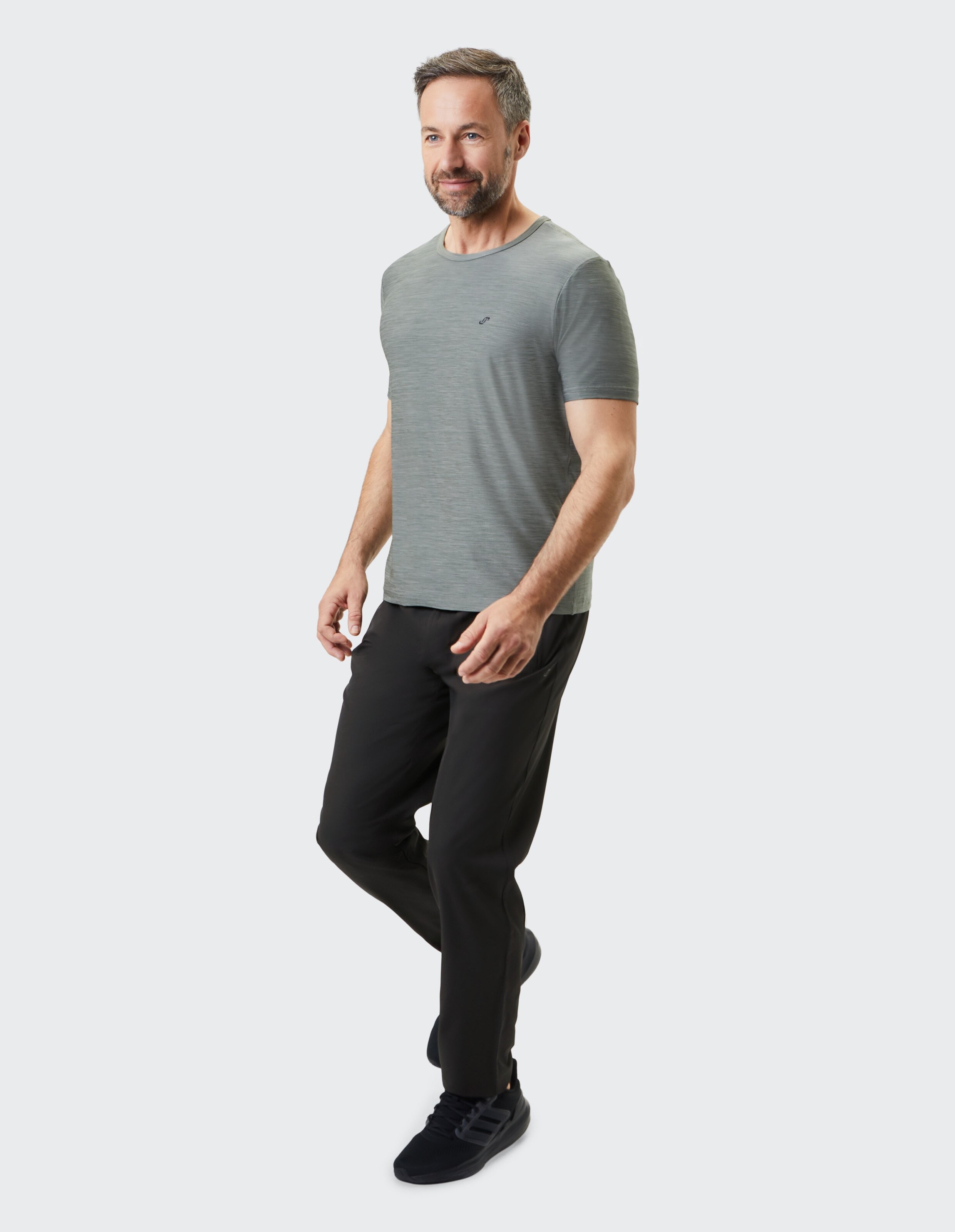 Ein lächelnder Mann in einem weißen T-Shirt und schwarzen Hosen macht einen Schritt