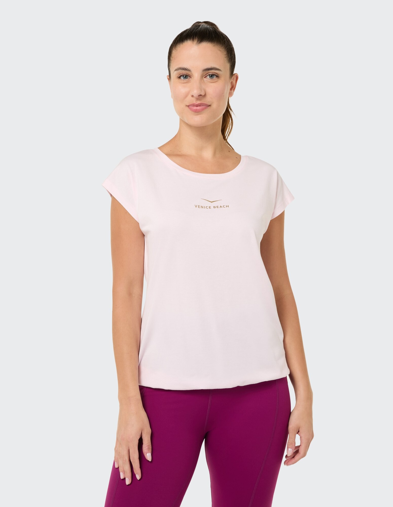 Hellrosa lässiges T-Shirt mit Venice Beach-Logo, gepaart mit lila Leggings.