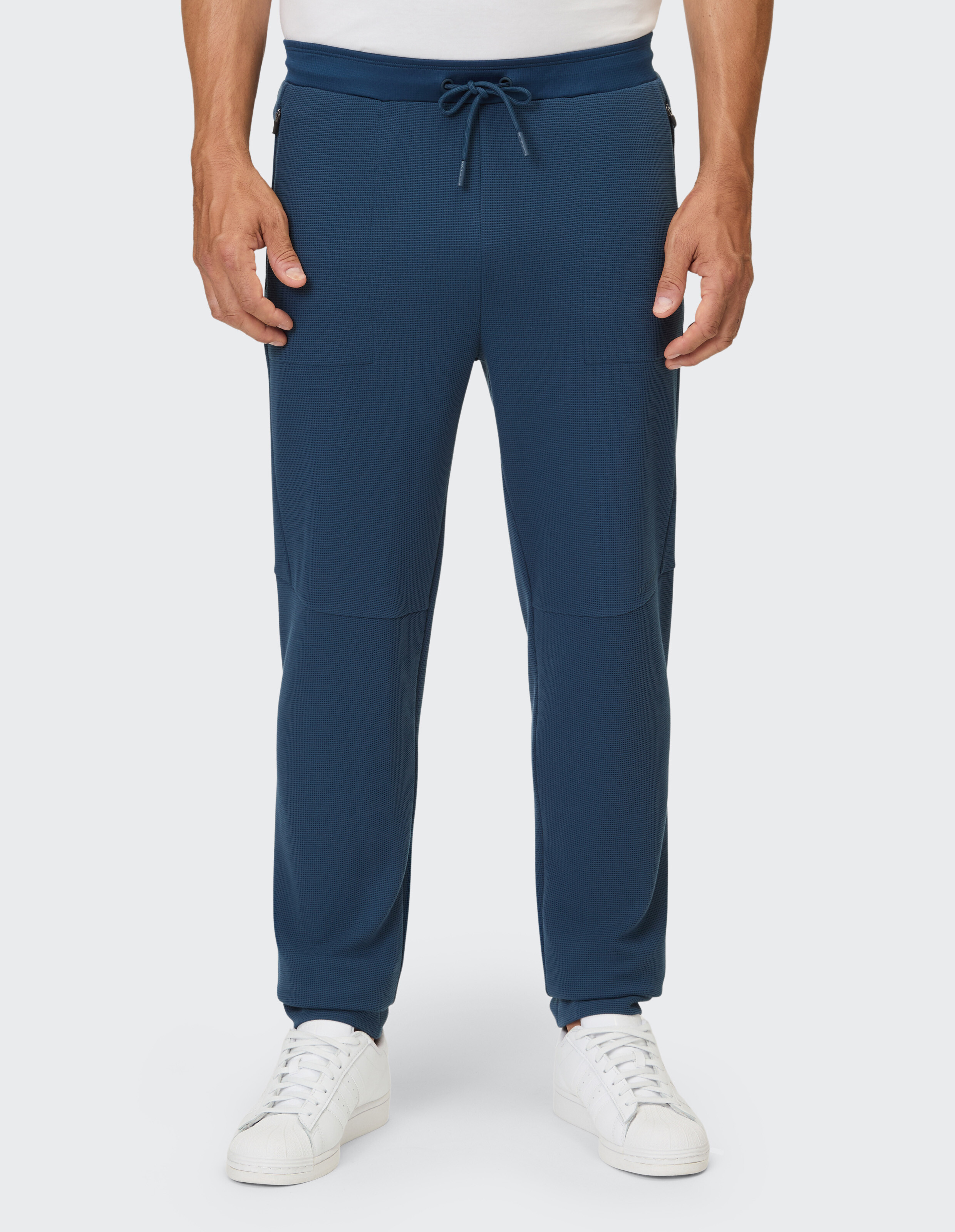 Lässige Herren-Jogginghose in Marineblau mit Taschen und Kordelzug in der Taille, gepaart mit weißen Turnschuhen.