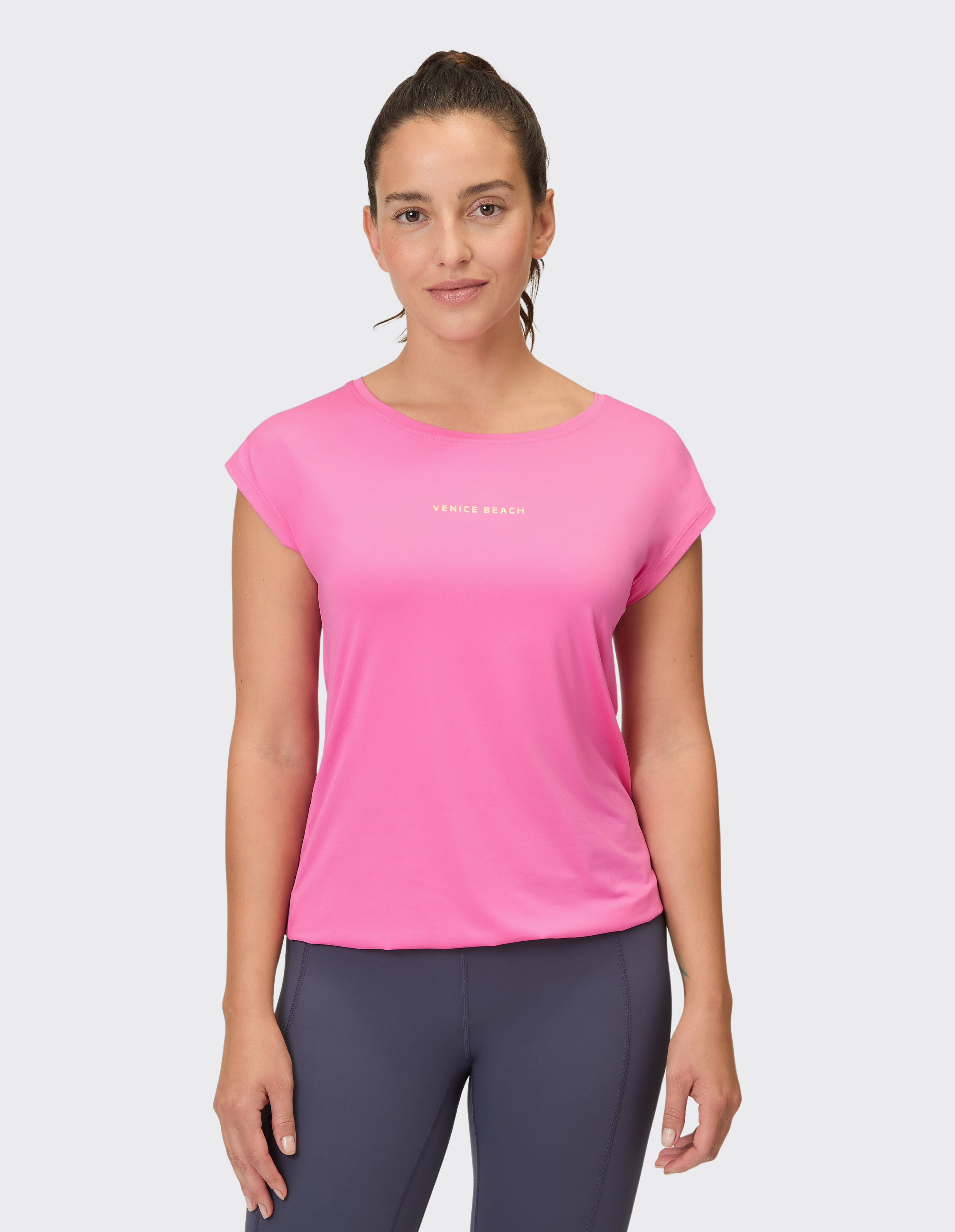 Frau trägt ein leuchtend rosafarbenes Venice Beach-Freizeit-T-Shirt für aktive Lounge-Kleidung.