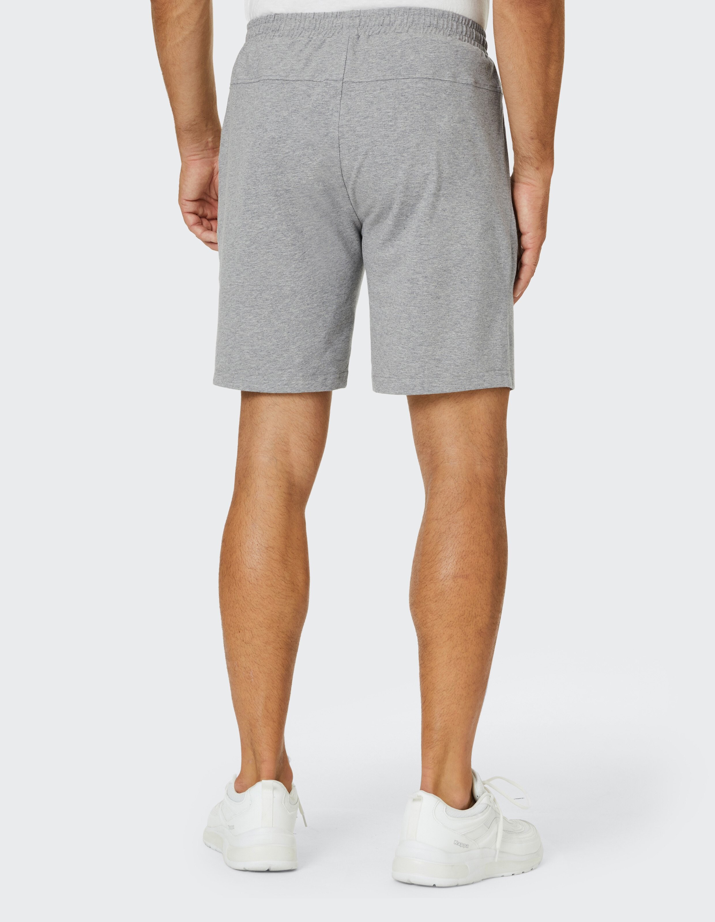 Rückansicht eines Mannes in grauen Shorts mit elastischem Bund und weißen Sportschuhen auf hellem Hintergrund.