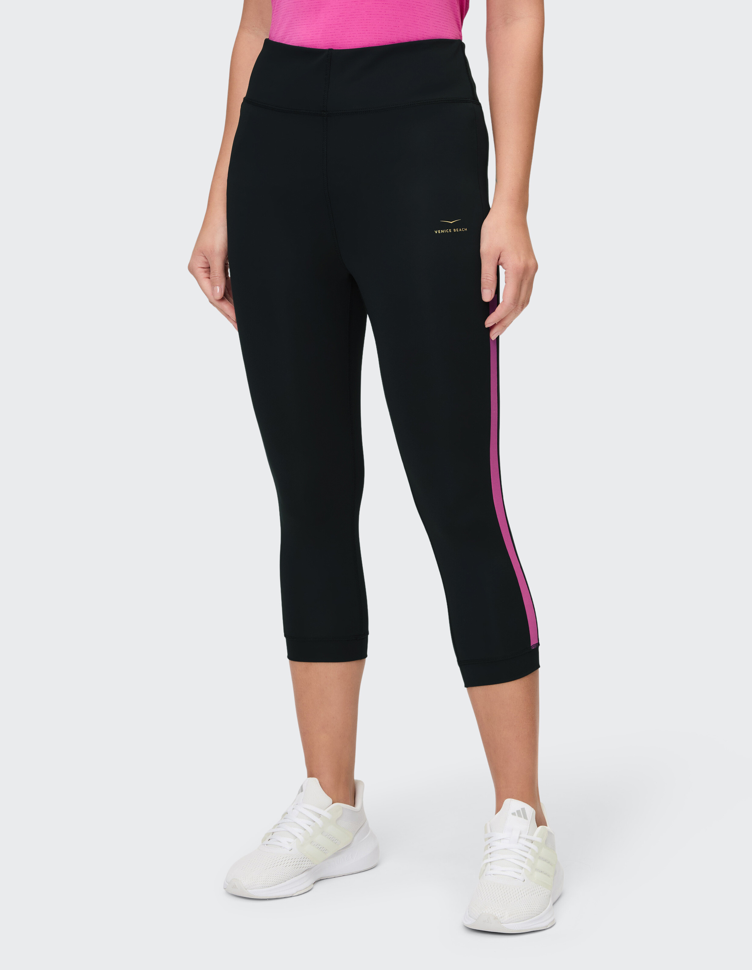 Schwarze Capri-Leggings mit rosa Seitenstreifen, gepaart mit einem rosa Top und weißen Sneakers.