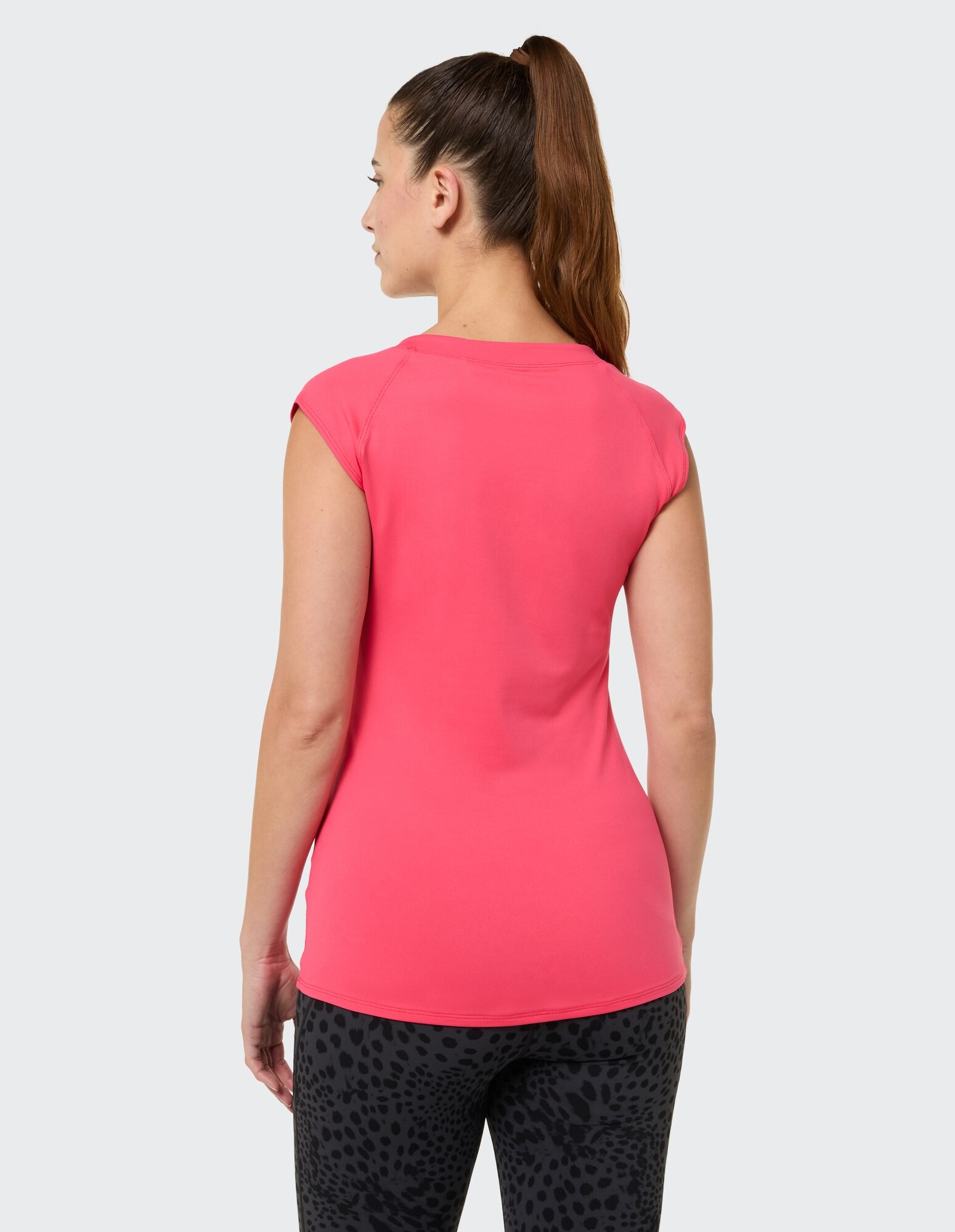 Rückansicht einer Frau in einem rosa Oberteil mit Flügelärmeln und schwarzen Leggings mit Leopardenmuster.