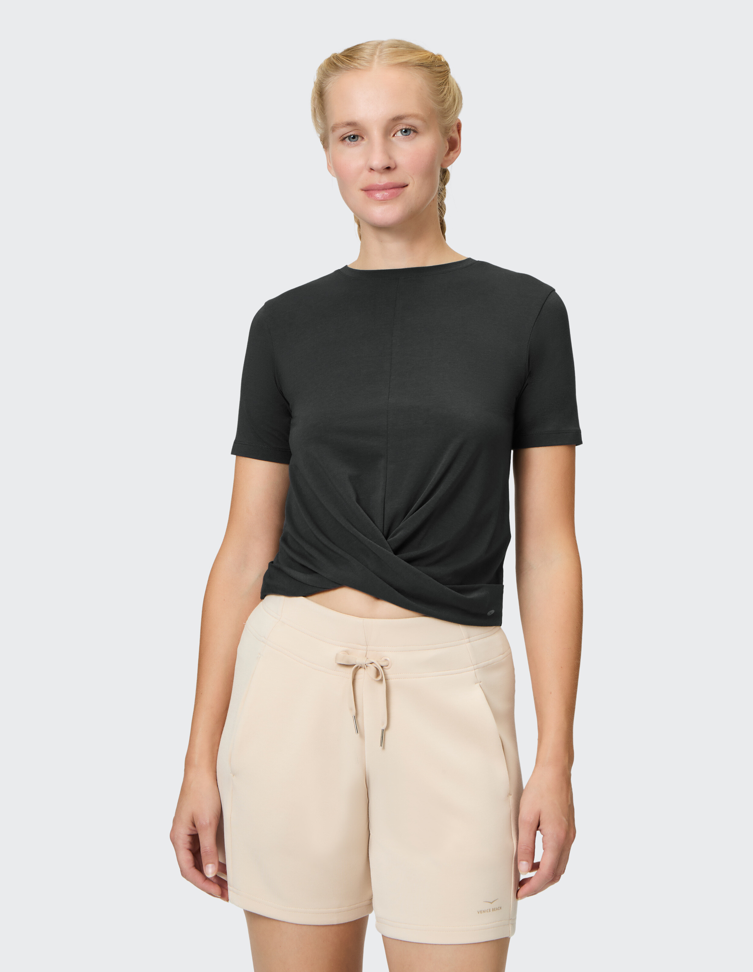 Frau in einem schwarzen T-Shirt mit Twist-Front und beigen Shorts, ideal für Freizeitkleidung.