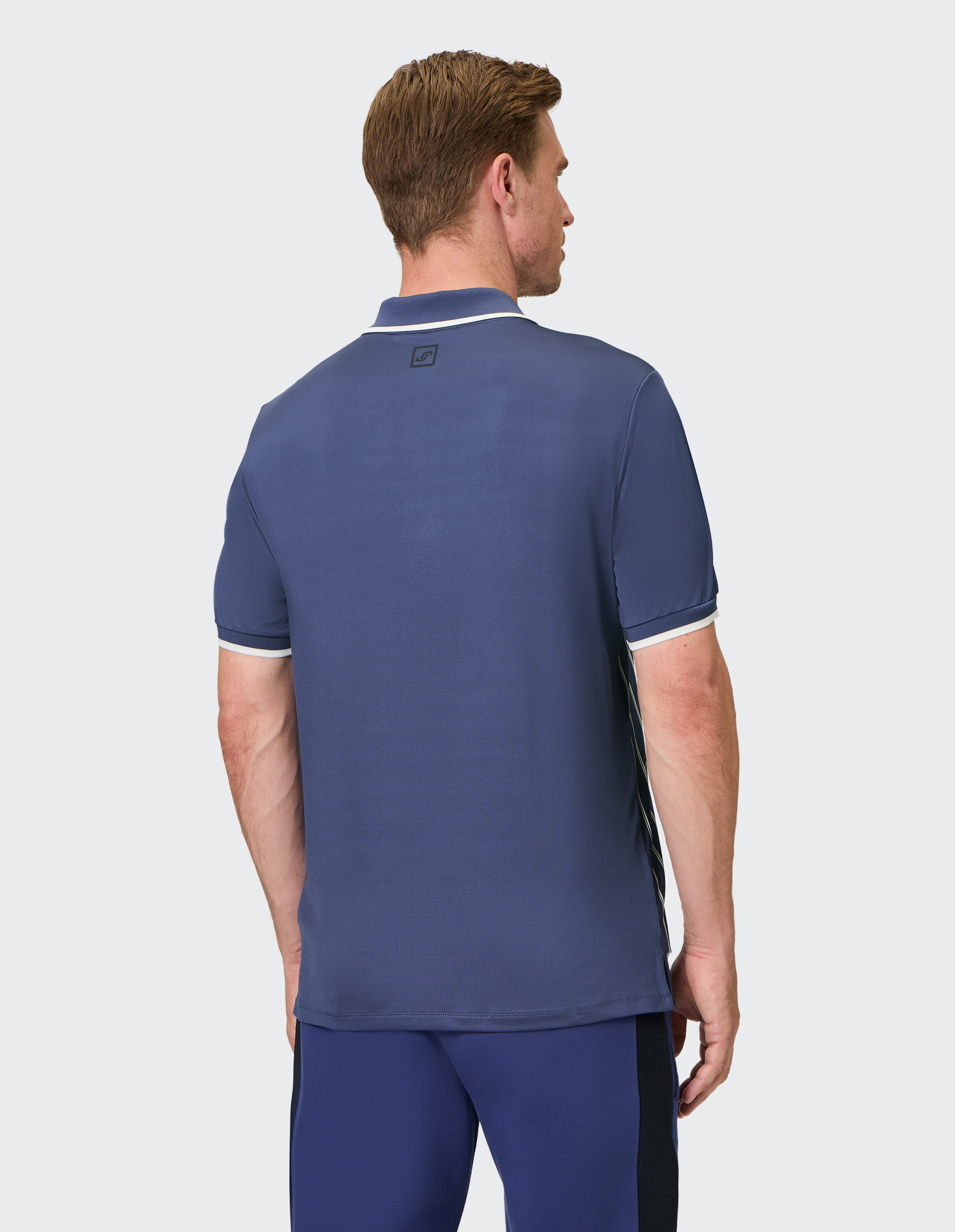 Mann trägt ein blaues ELBSAND-Poloshirt mit weißem Besatz, Rückansicht, lässiger Stil.