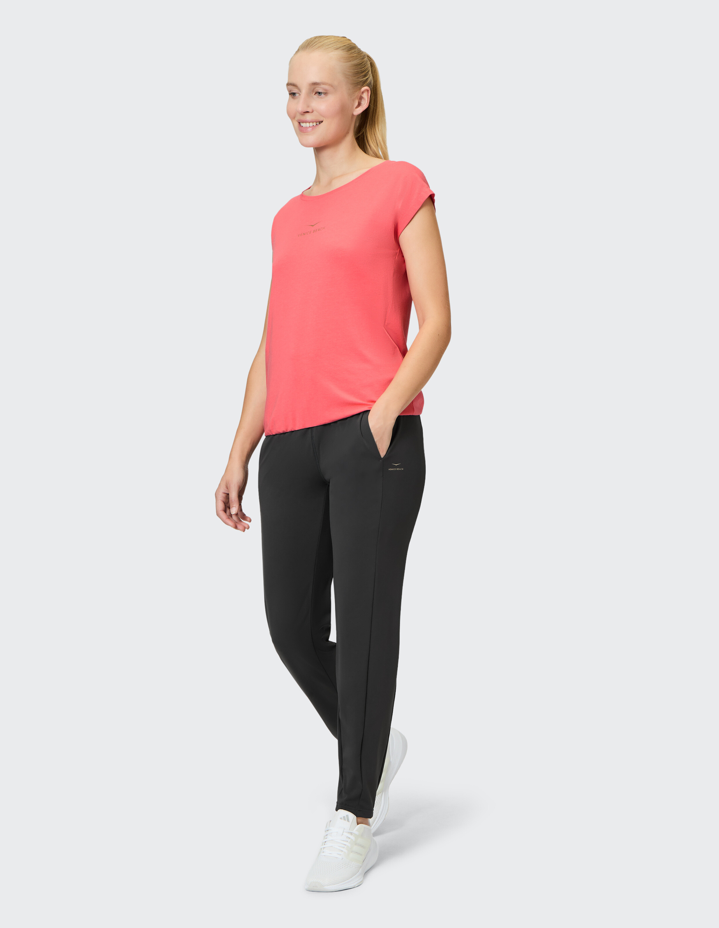 Frau trägt ein korallenrotes T-Shirt und eine schwarze Freizeithose für einen bequemen Lounge-Look.