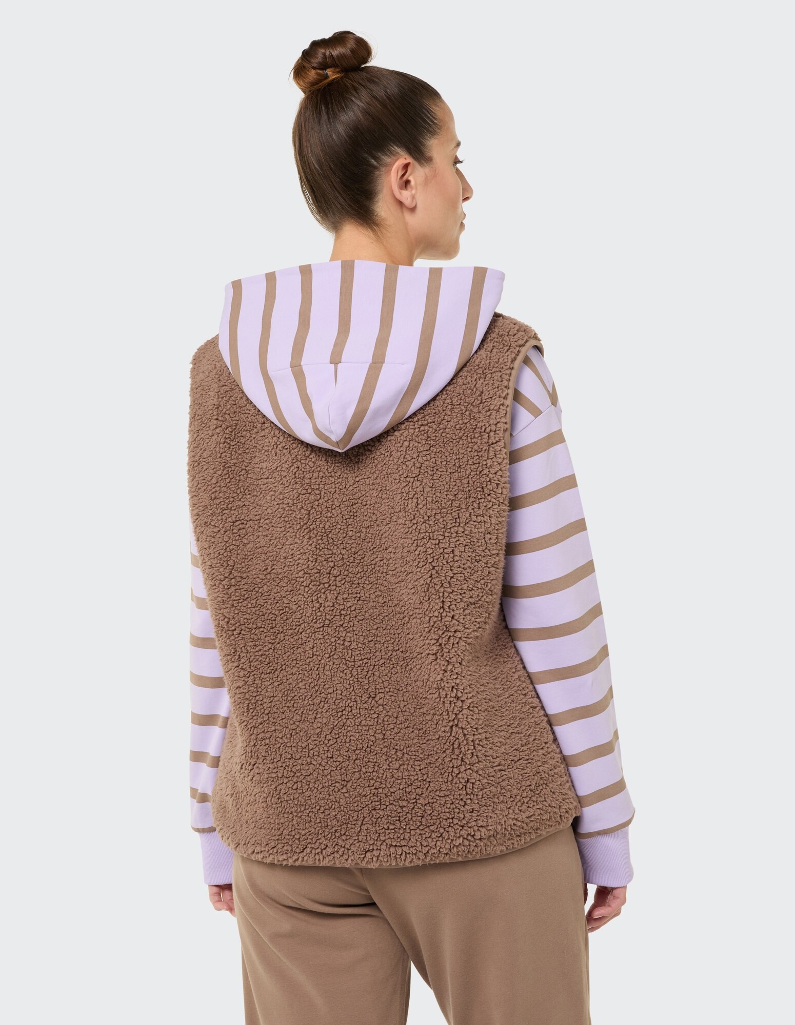 Kuschelige braune Fleeceweste über einem gestreiften Kapuzenpullover, perfekt für Freizeitkleidung.