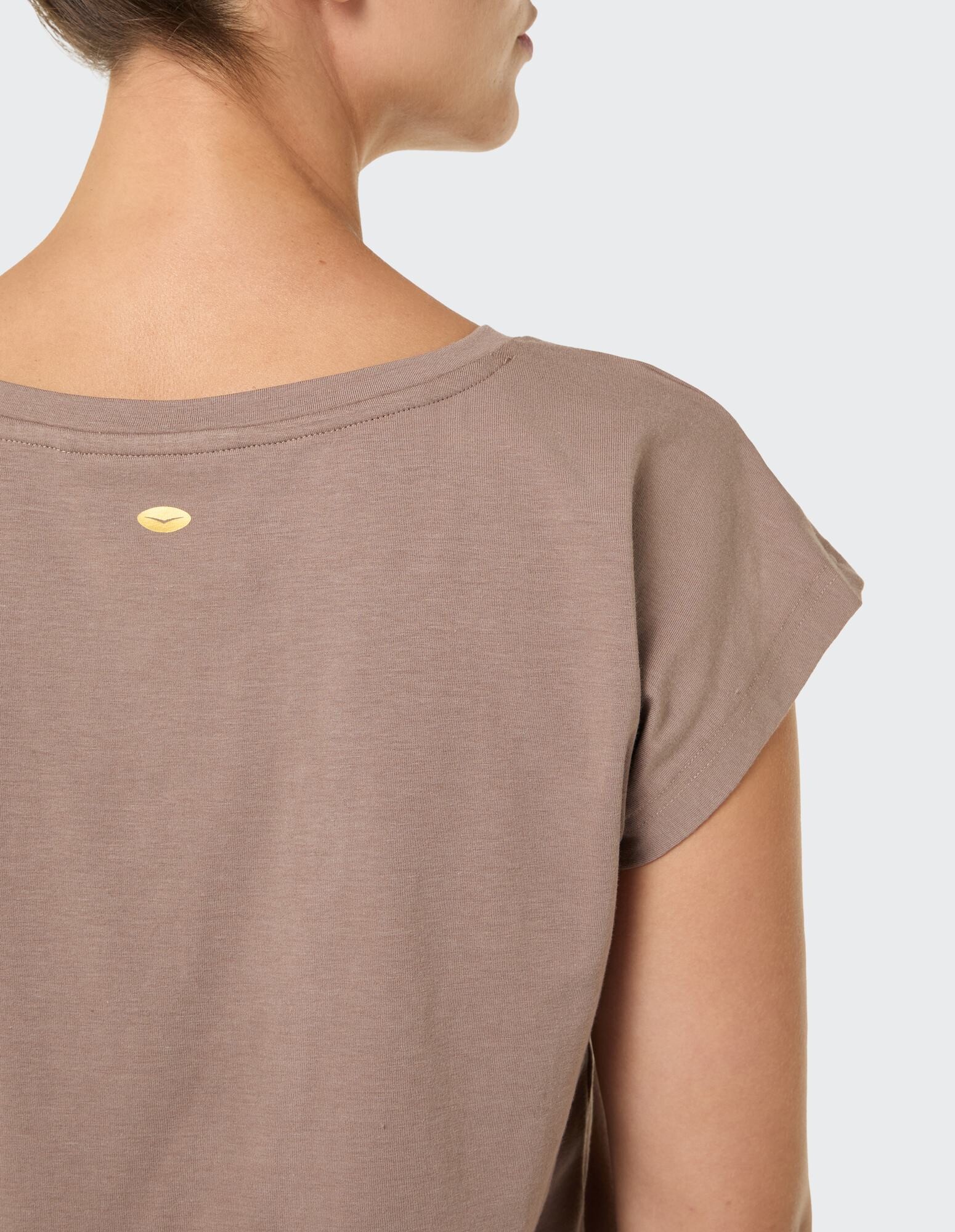 Rückansicht einer Frau, die ein gemütliches taupefarbenes Freizeit-T-Shirt mit kurzen Ärmeln trägt.