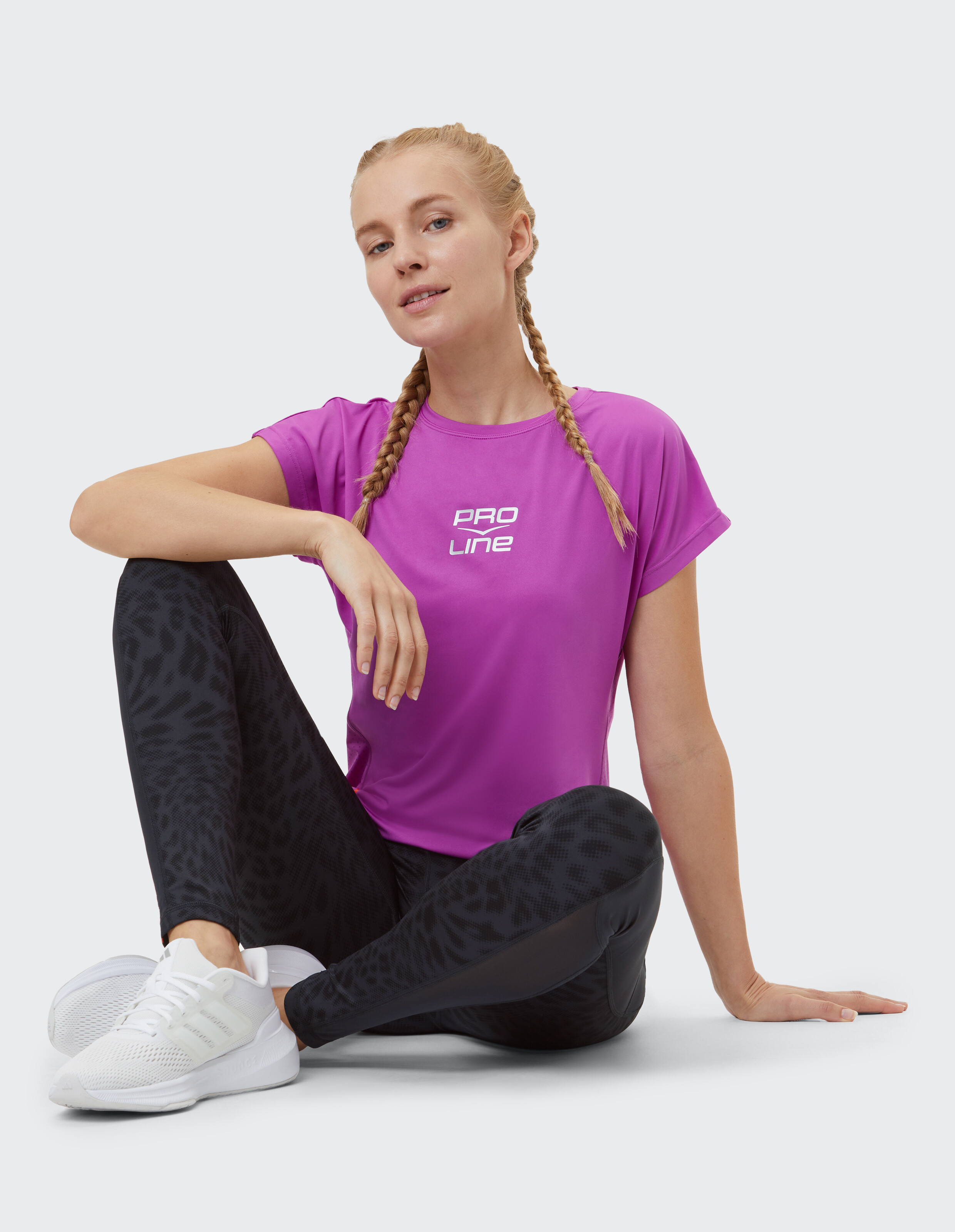 Frau in rosa PRO LINE-T-Shirt und schwarz gemusterten Leggings sitzt lässig.
