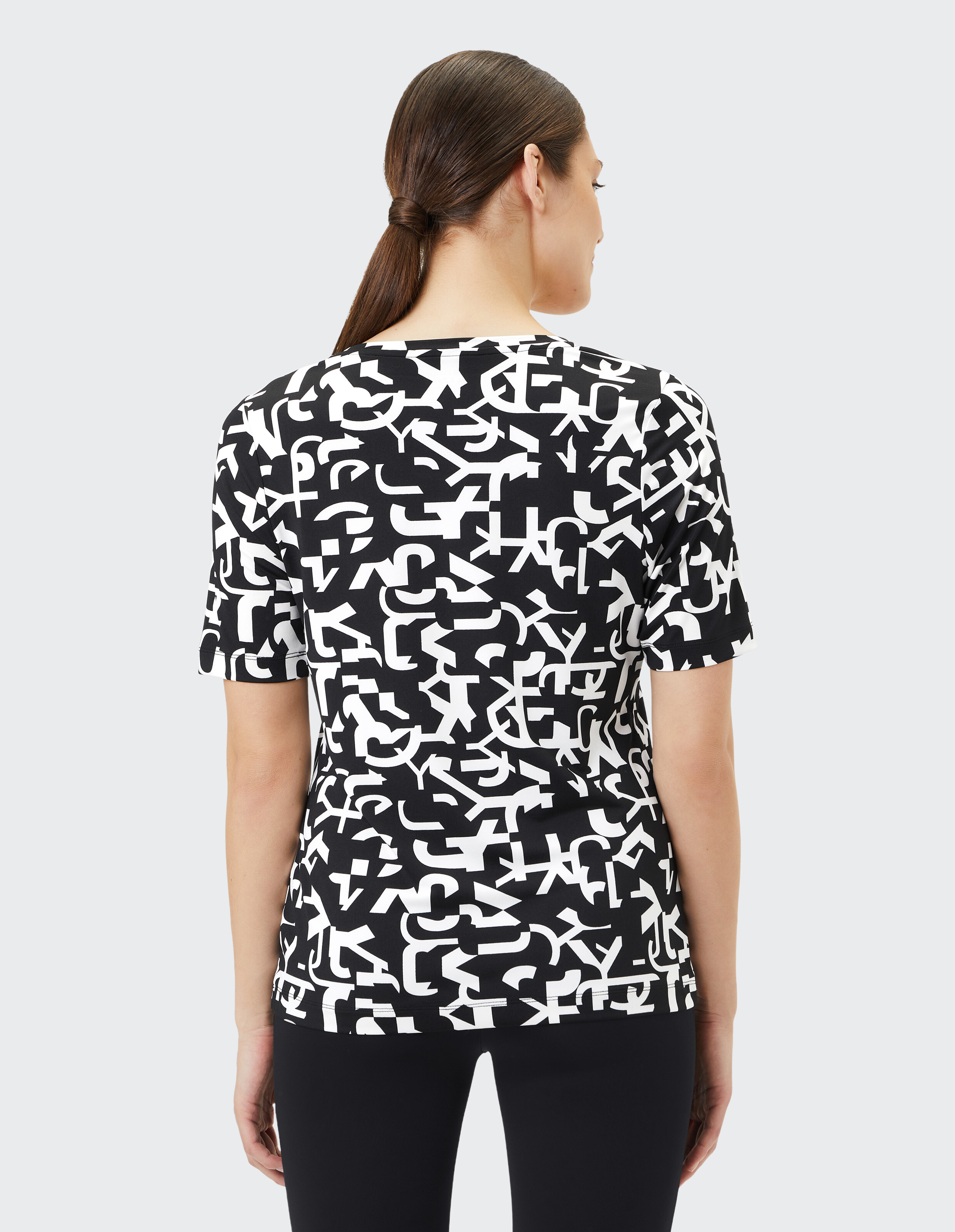 Schwarzes T-Shirt mit weißem, abstraktem Buchstabenmuster, das aus verschiedenen, überlappenden Buchstaben besteht.