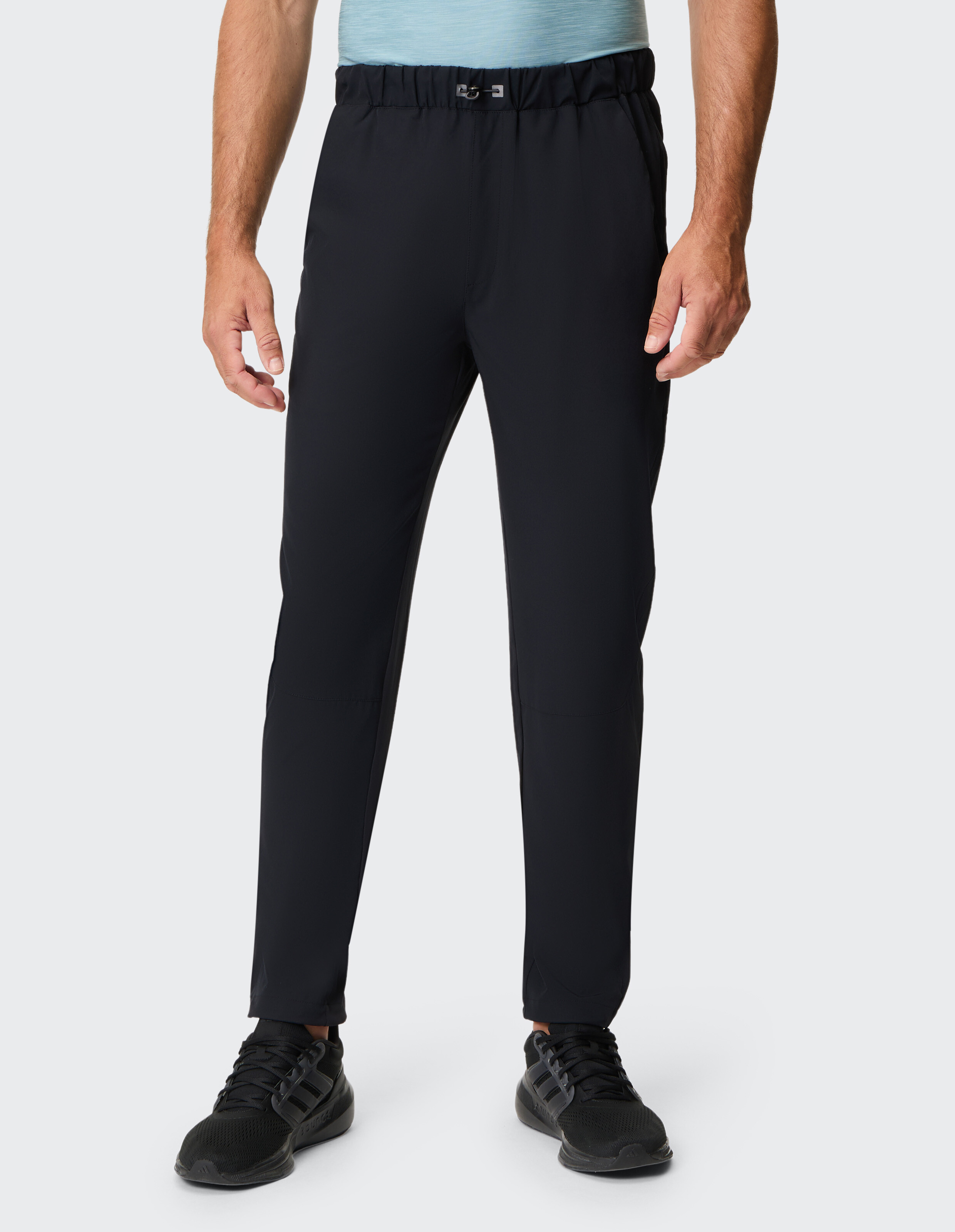 Ein Mann trägt eine schwarze Jogginghose mit elastischem Bund und schwarzen Sneakers, begleitet von einem hellblauen T-Shirt.