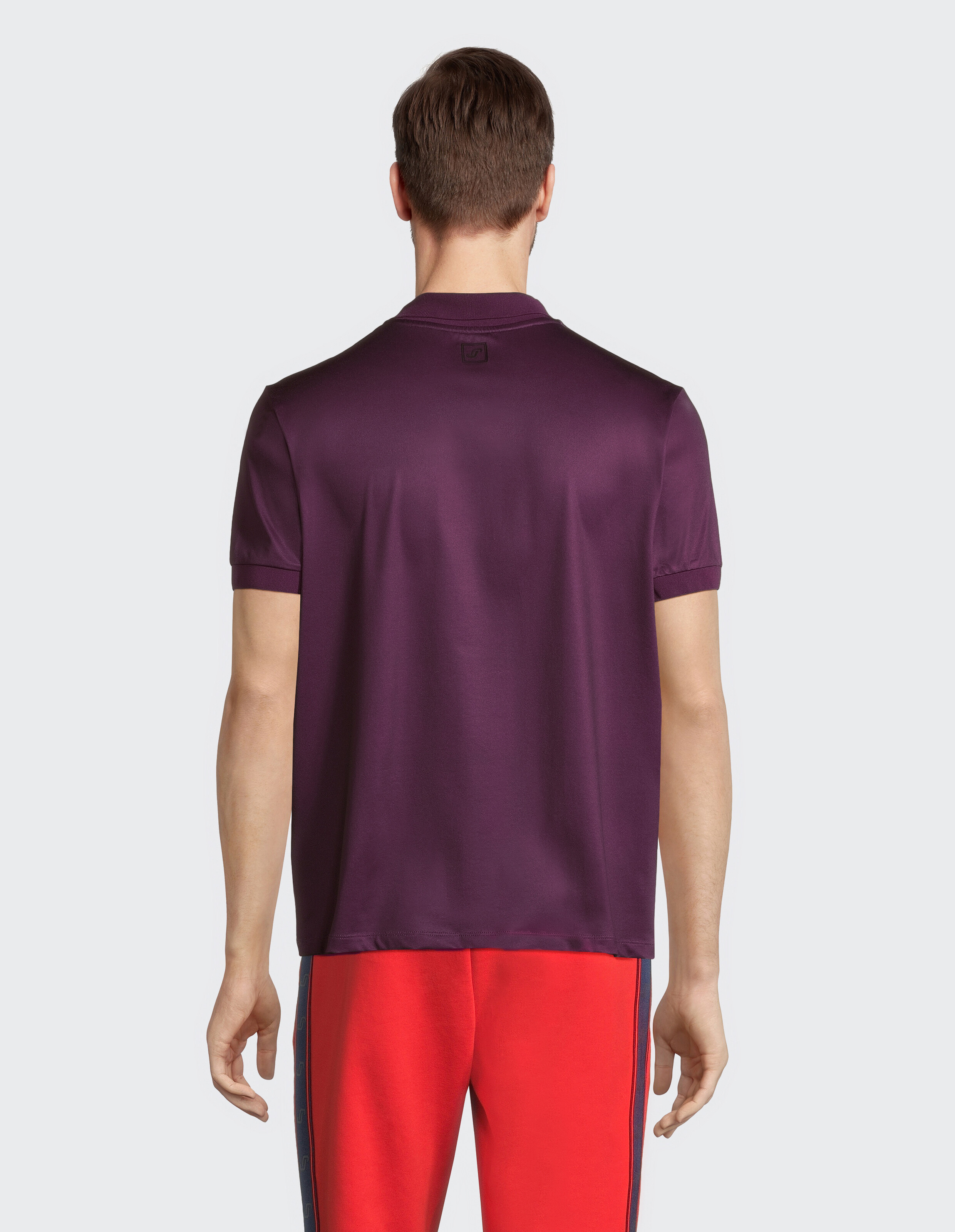 Mann trägt ein lila Poloshirt und eine rote Freizeithose von hinten.