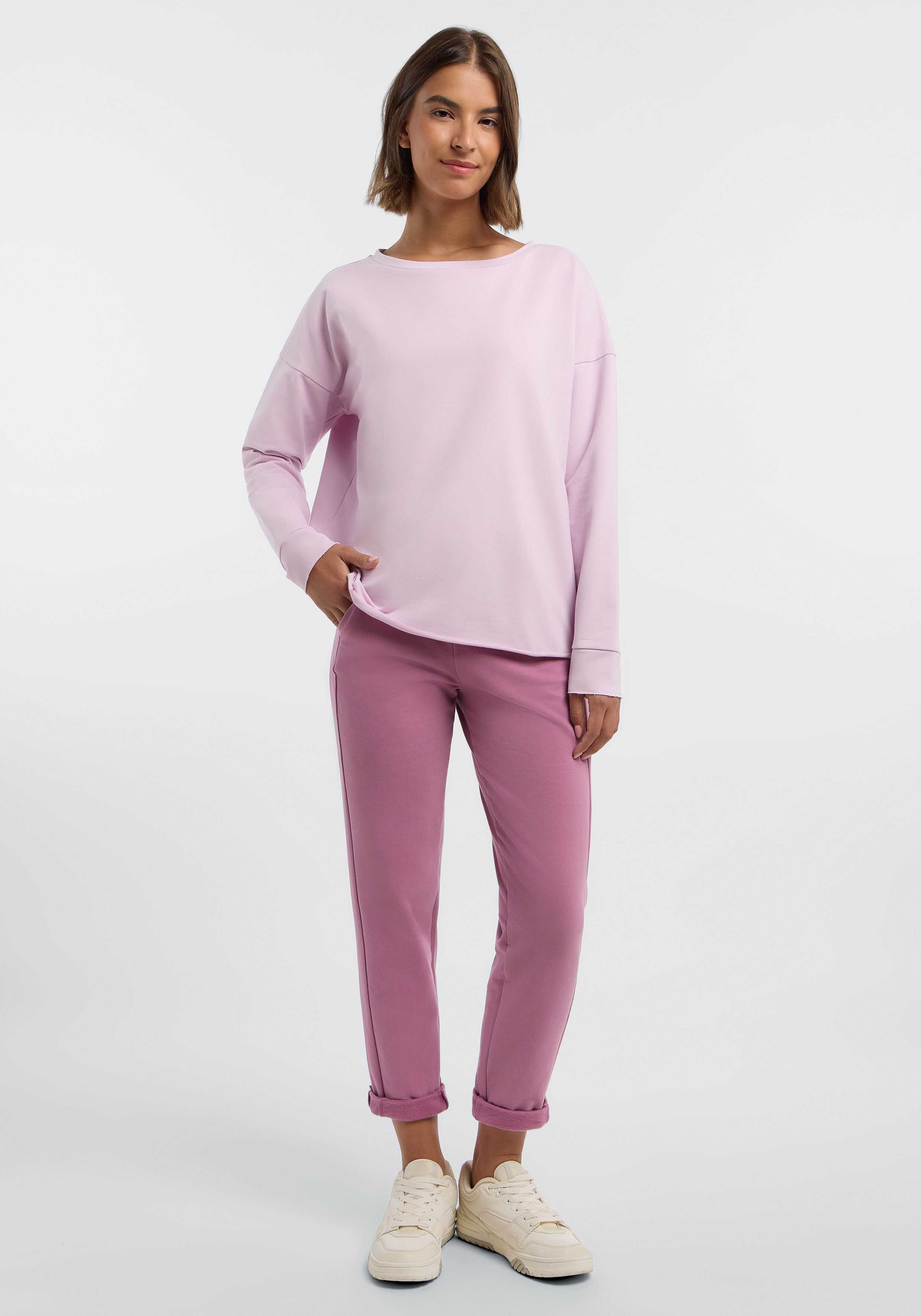 Frau trägt ein hellrosa Langarm-Sweatshirt und eine passende Freizeithose.