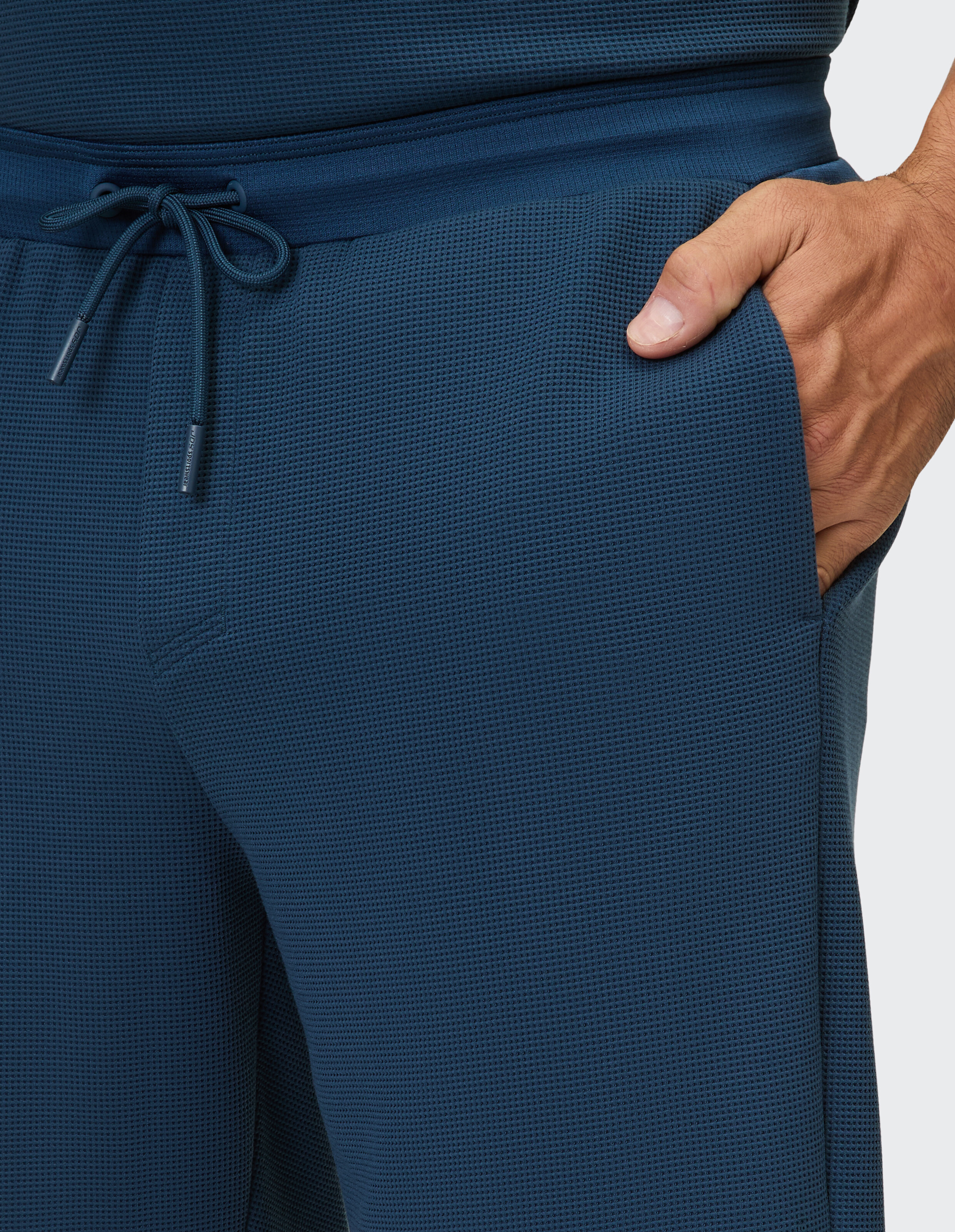 Marineblaue Hose mit Waffelmuster und Kordelzug, in die eine Hand hineingesteckt ist.