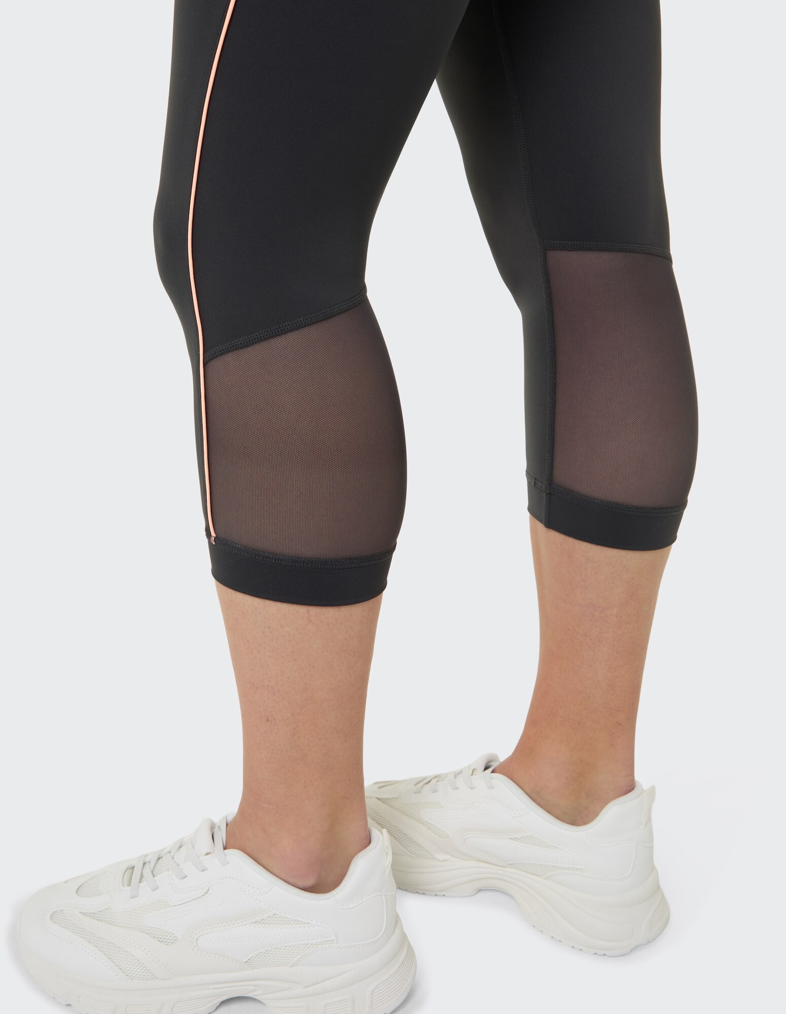 Schwarze Capri-Leggings mit Mesh-Einsätzen und rosa Akzenten, gepaart mit weißen Sneakers.