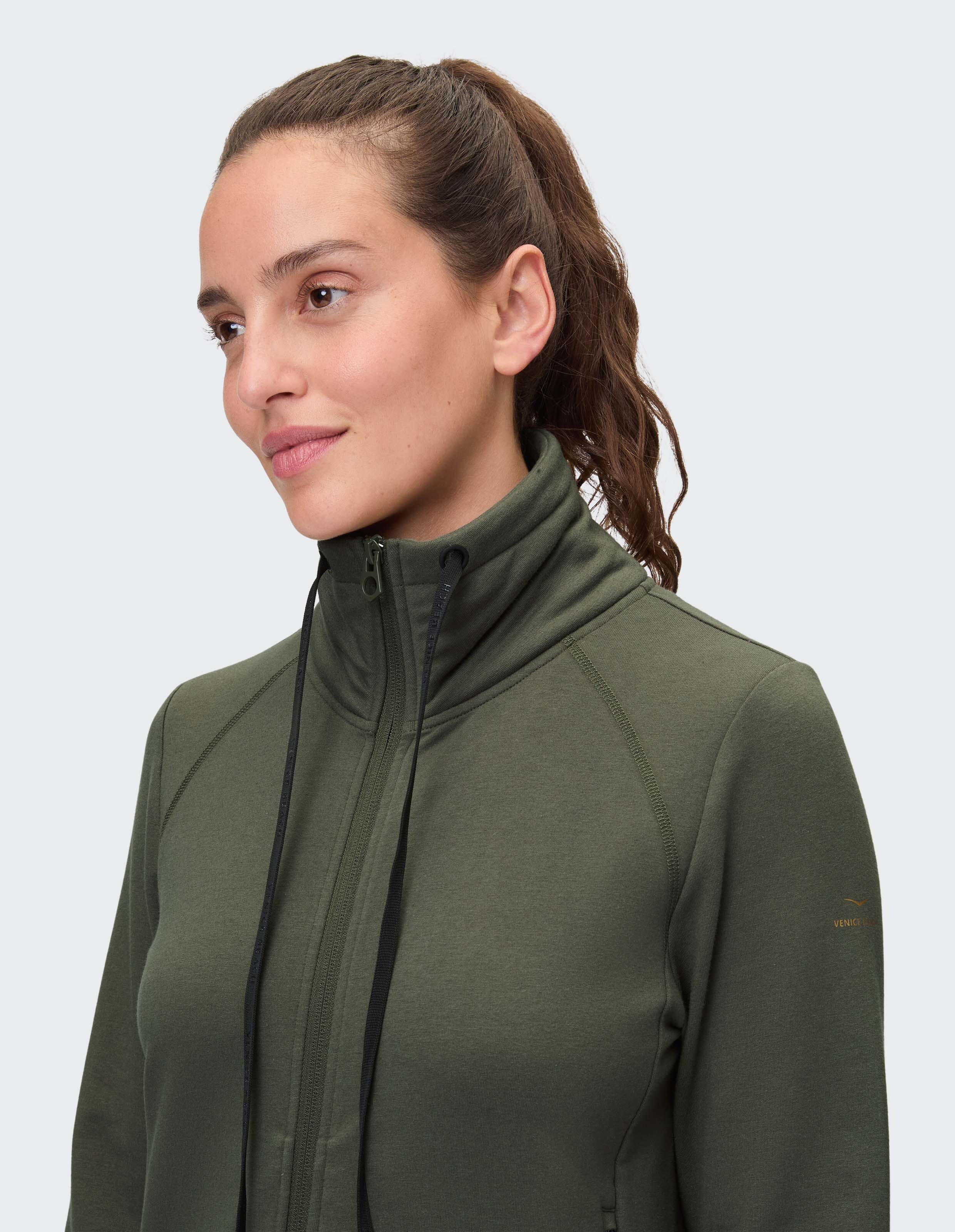 Nahaufnahme einer Frau in einer grünen Jacke mit Reißverschluss, hohem Kragen und Kordelzug.
