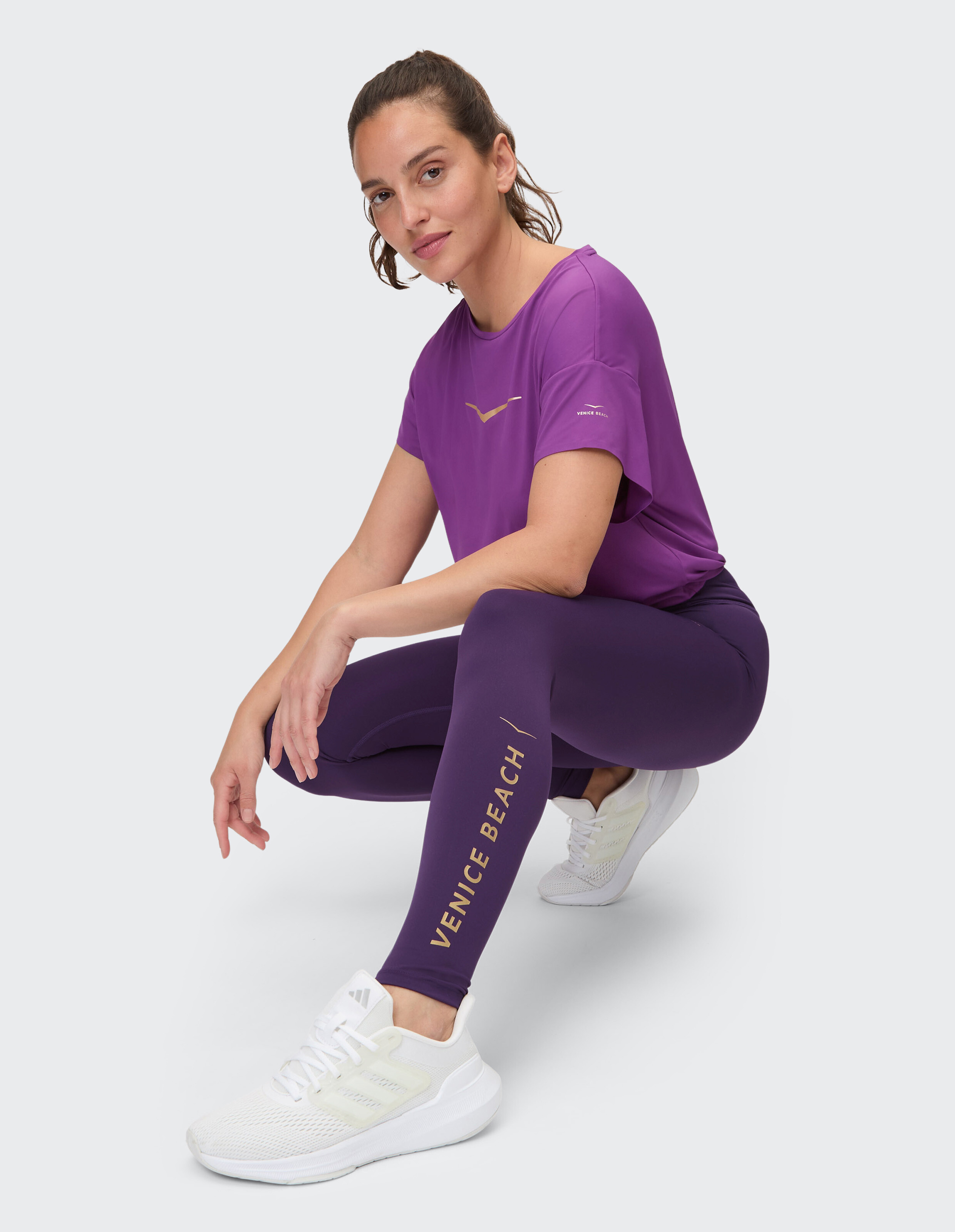 Frau in lilafarbenem Venice Beach Activewear-T-Shirt und Leggings kauert.