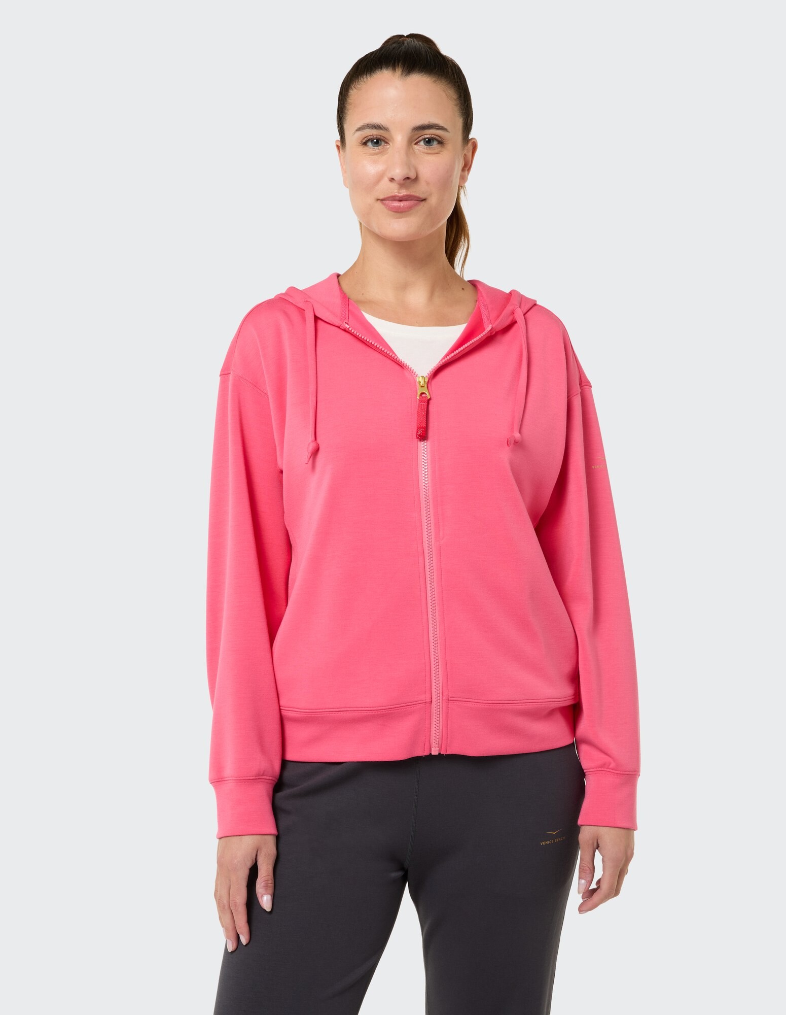 Frau trägt einen rosa Kapuzenpullover mit Reißverschluss, perfekt zum entspannten Faulenzen oder Reisen.