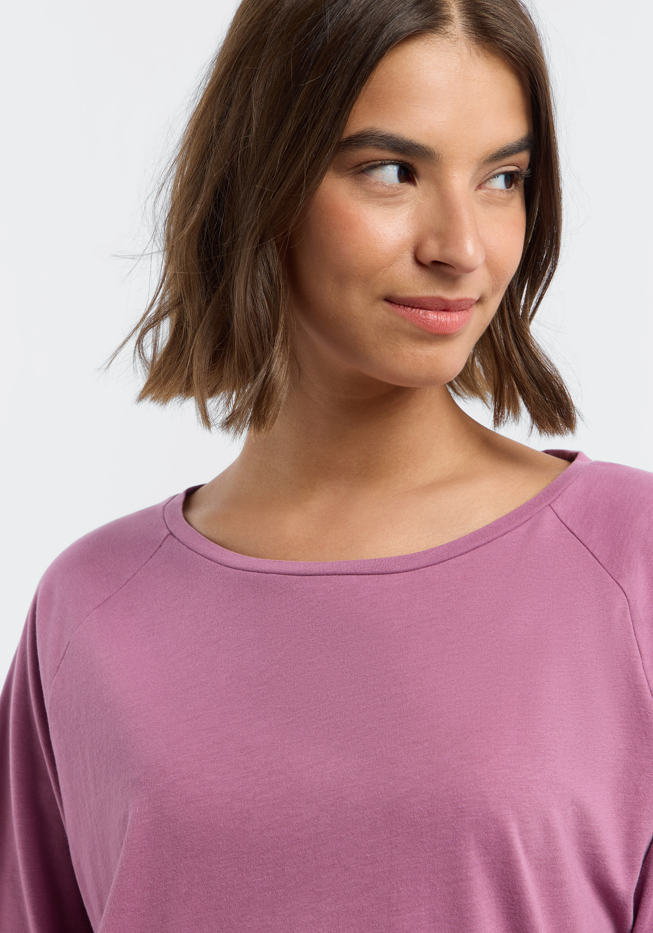 Frau trägt ein gemütliches, mauvefarbenes, lässiges Langarmshirt mit Raglanärmeln.