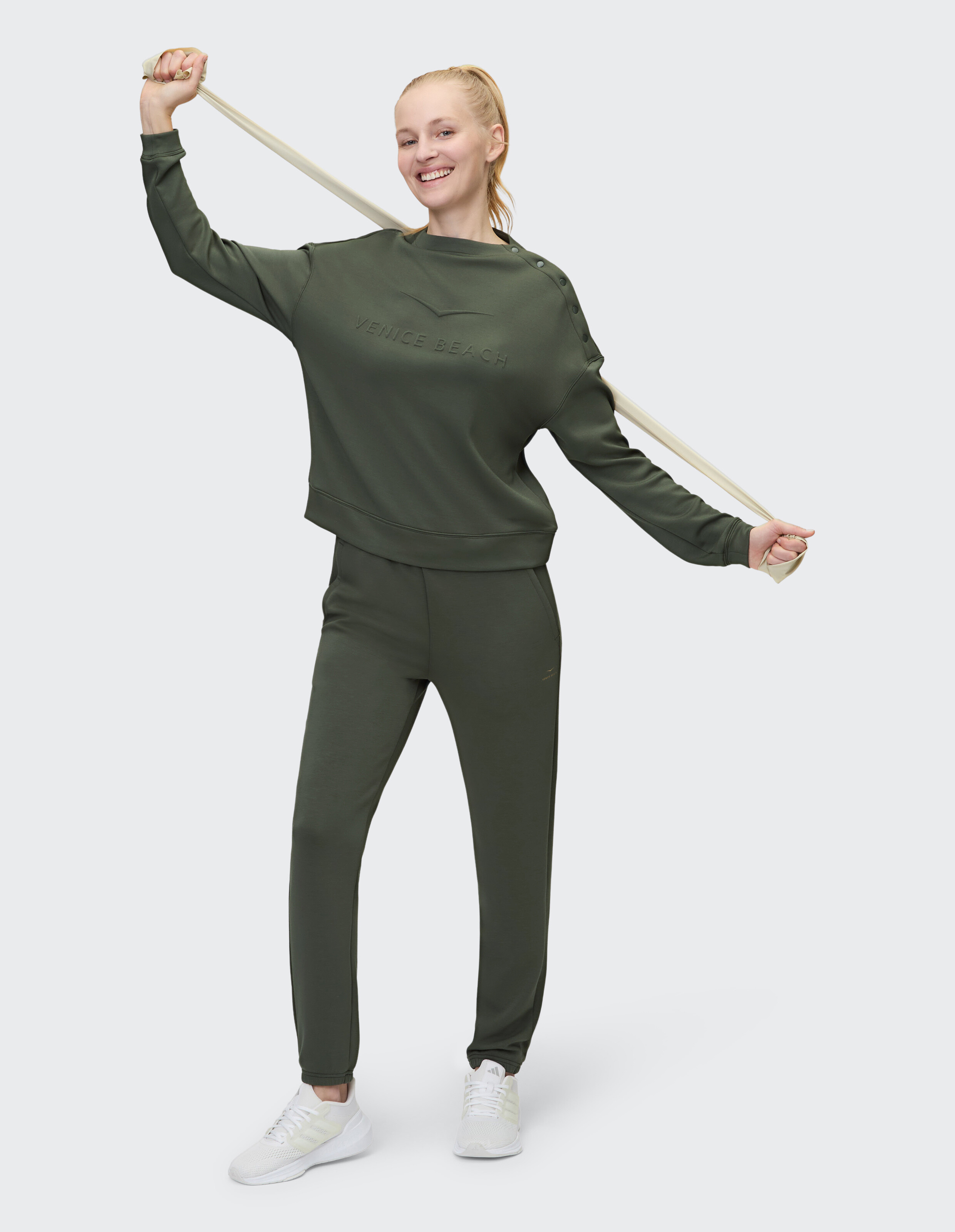 Lächelnde Frau in olivgrünem, lässigem Sweatshirt und Hose, die Komfort und Stil zur Schau stellt.