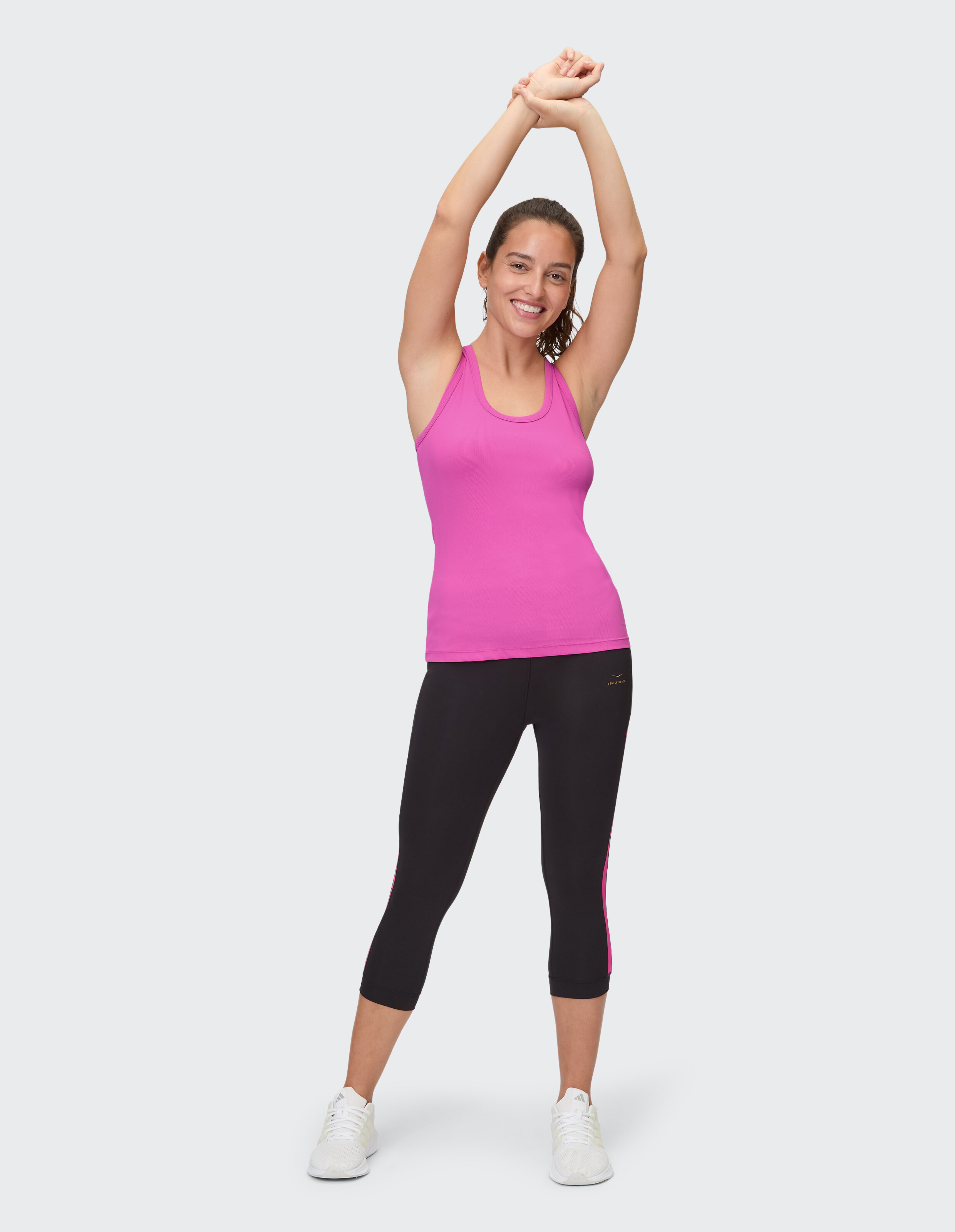 Frau in rosa Tanktop und schwarzen Capri-Leggings streckt sich fröhlich.