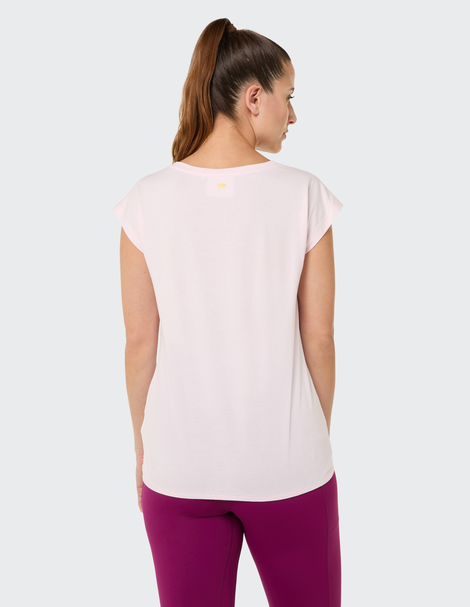 Rückansicht einer Frau in einem hellrosa Freizeittop und lila Leggings.