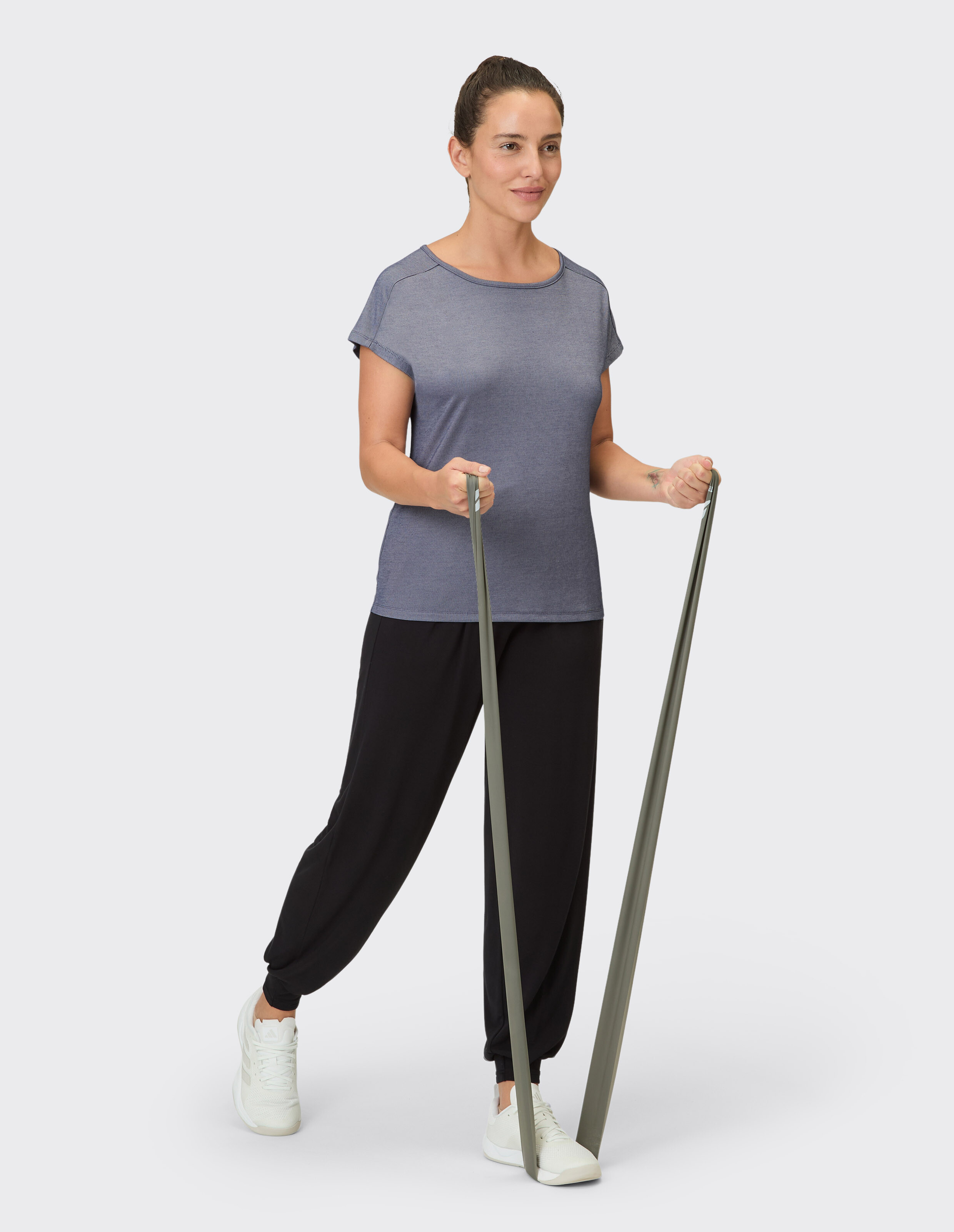 Frau in einem lässigen grauen Top und schwarzen Jogginghosen, hält Widerstandsbänder in der Hand.