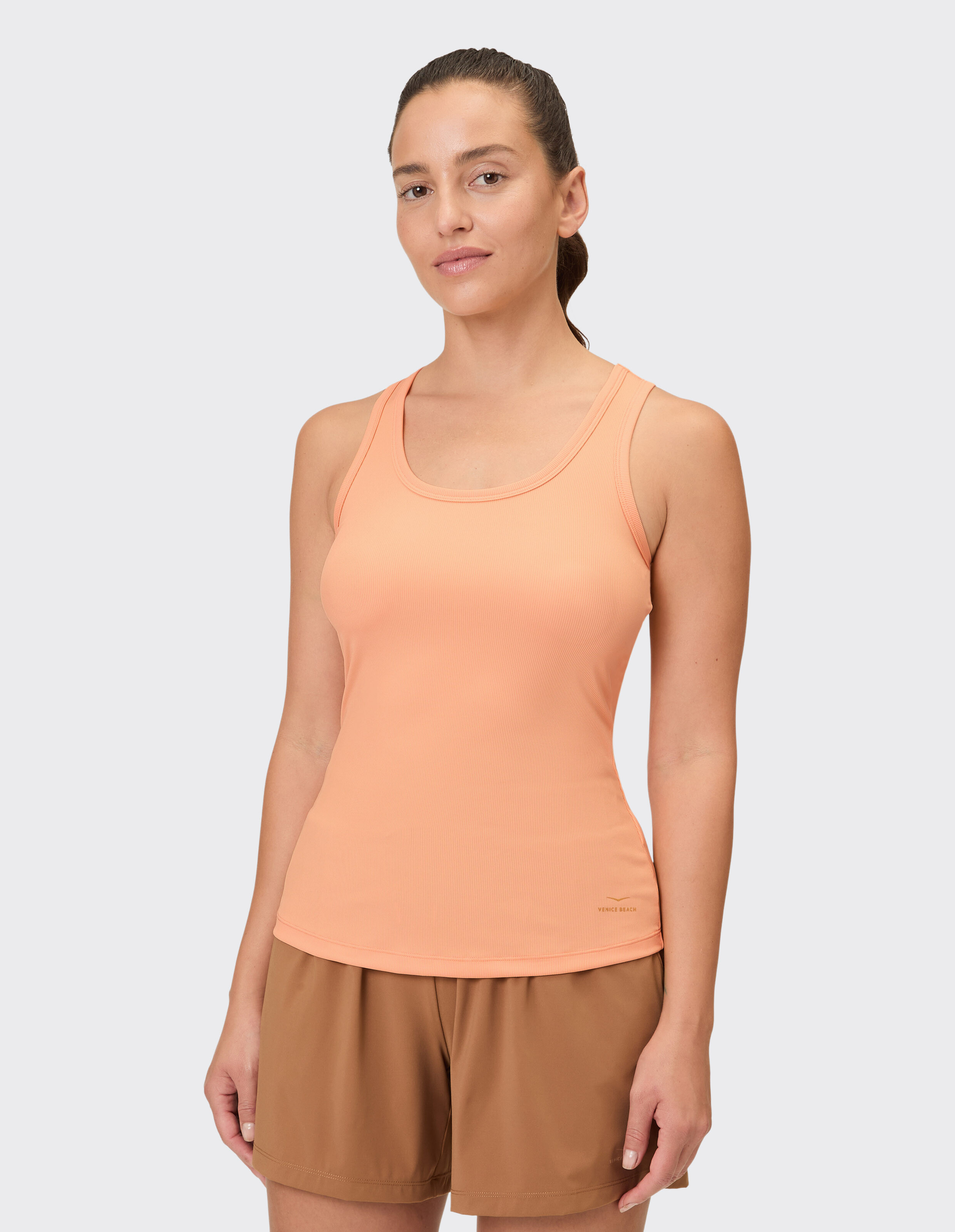 Frau trägt ein pfirsichfarbenes Tanktop und braune Shorts, ideal für Freizeitkleidung.