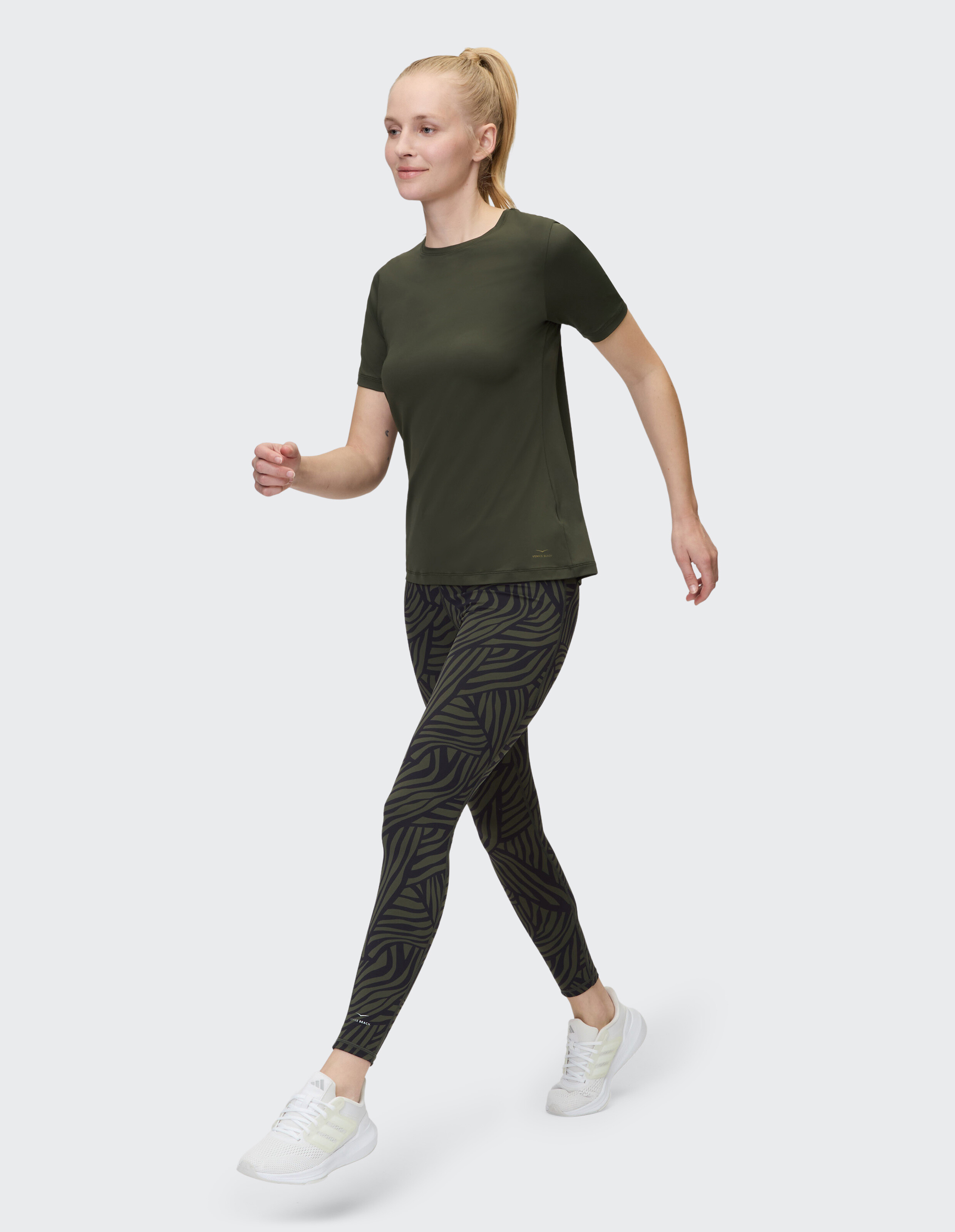 Frau in olivgrünem T-Shirt und gemusterten Leggings, die im lässigen Stil spaziert.