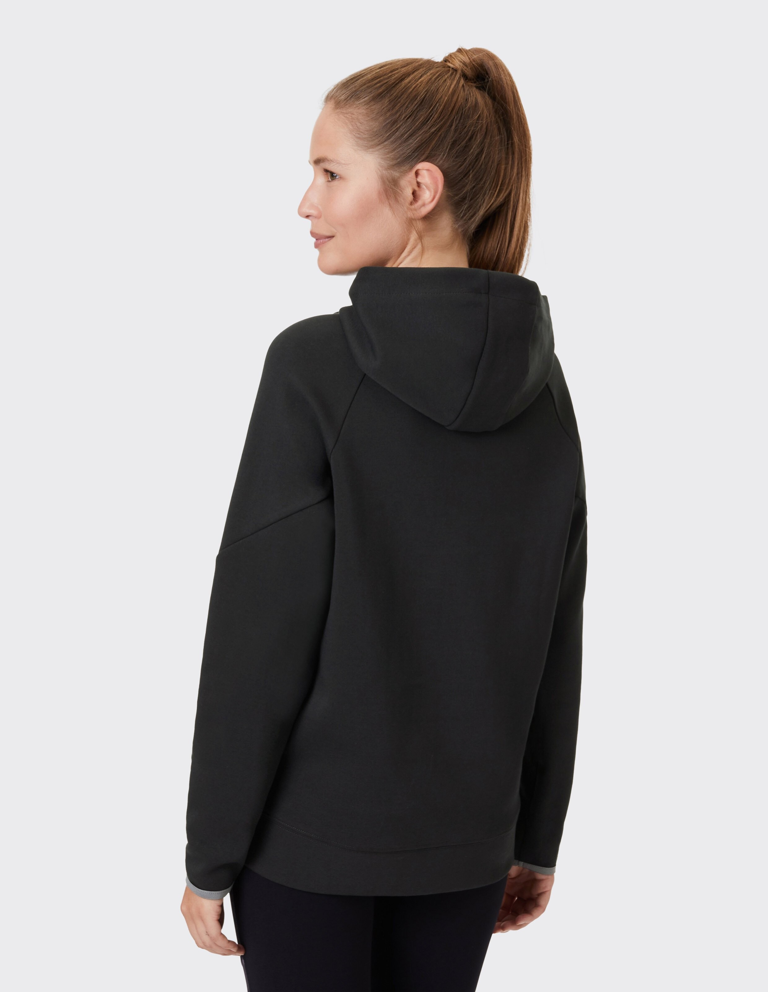Frau trägt einen kuscheligen schwarzen Kapuzenpullover mit entspannter Passform und Kapuzendesign.