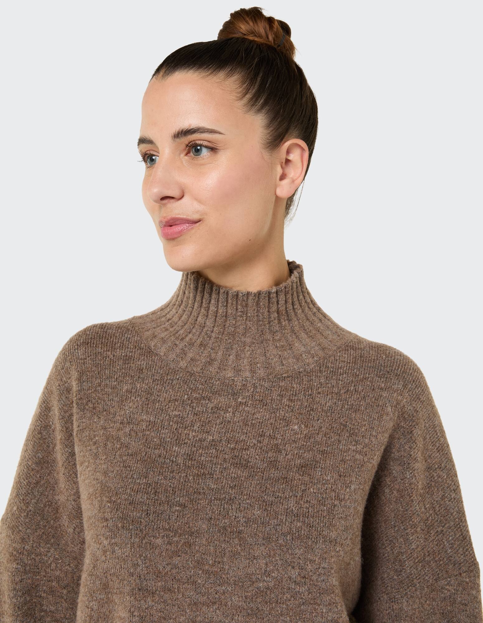 Nahaufnahme einer Frau in einem kuscheligen braunen Rollkragenpullover mit weicher Textur.