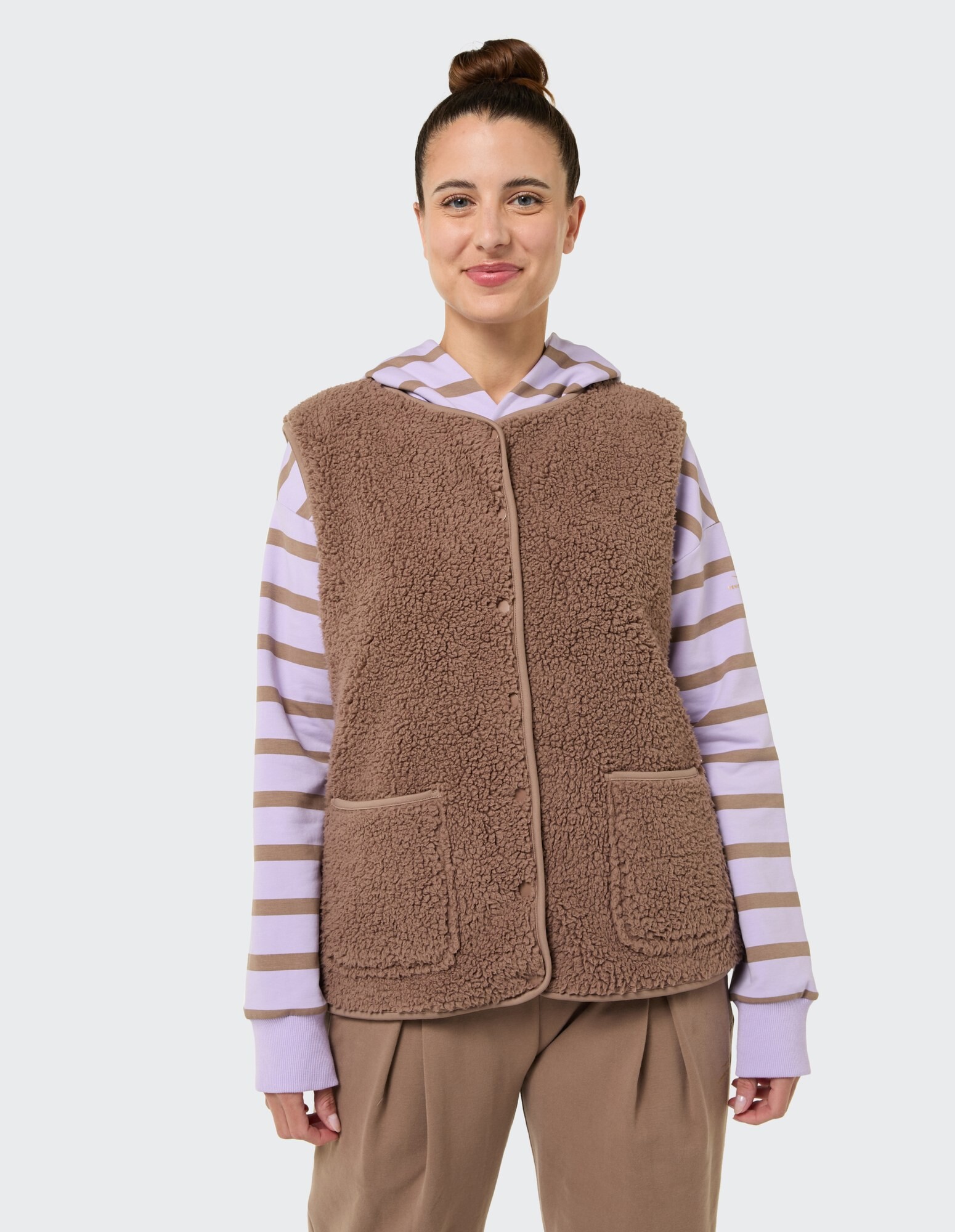 Kuschelige braune Fleeceweste über einem gestreiften Kapuzenpullover, perfekt für Freizeitkleidung.