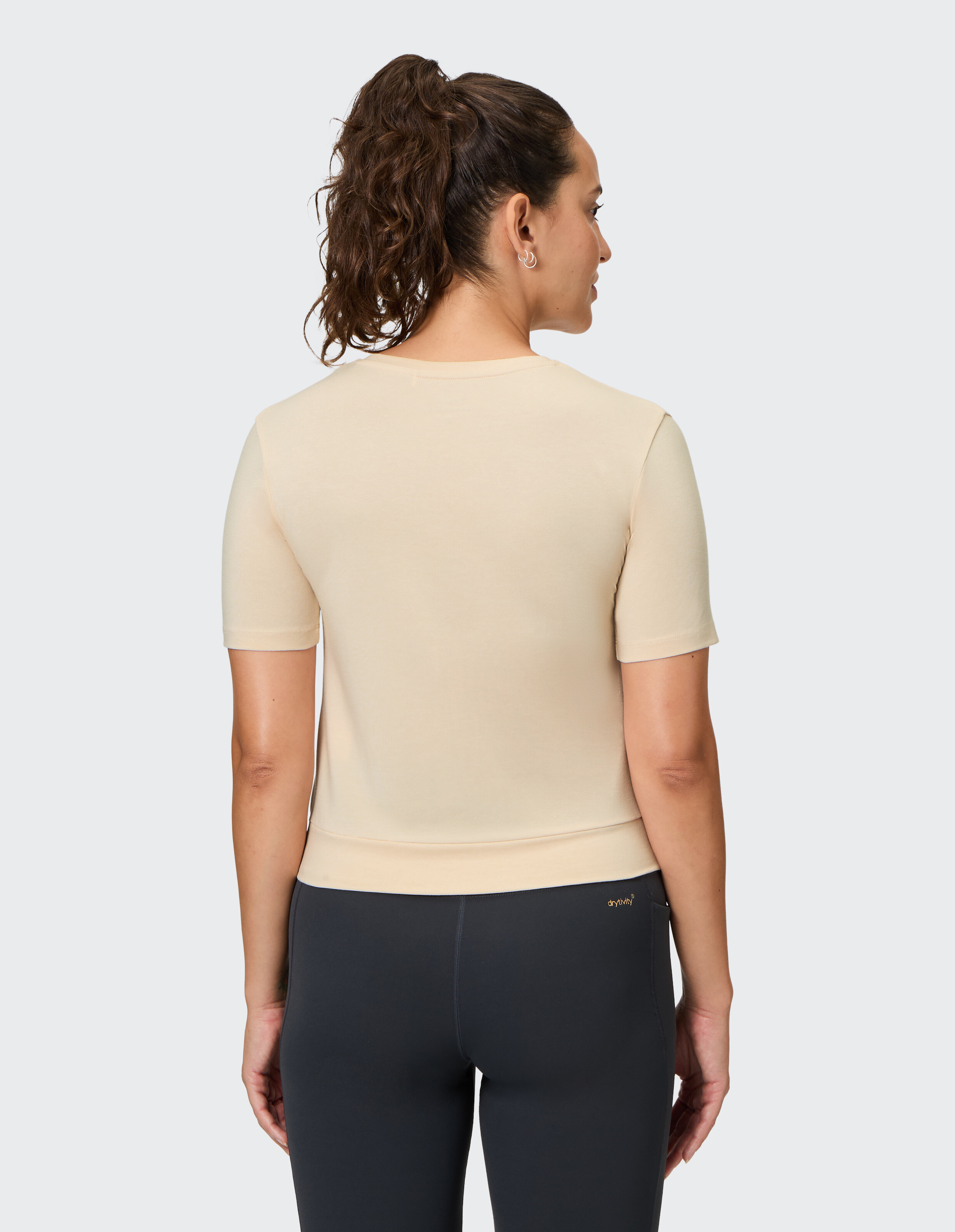 Rückansicht einer Frau in einem beigen Kurzarm-Top und schwarzen Leggings.