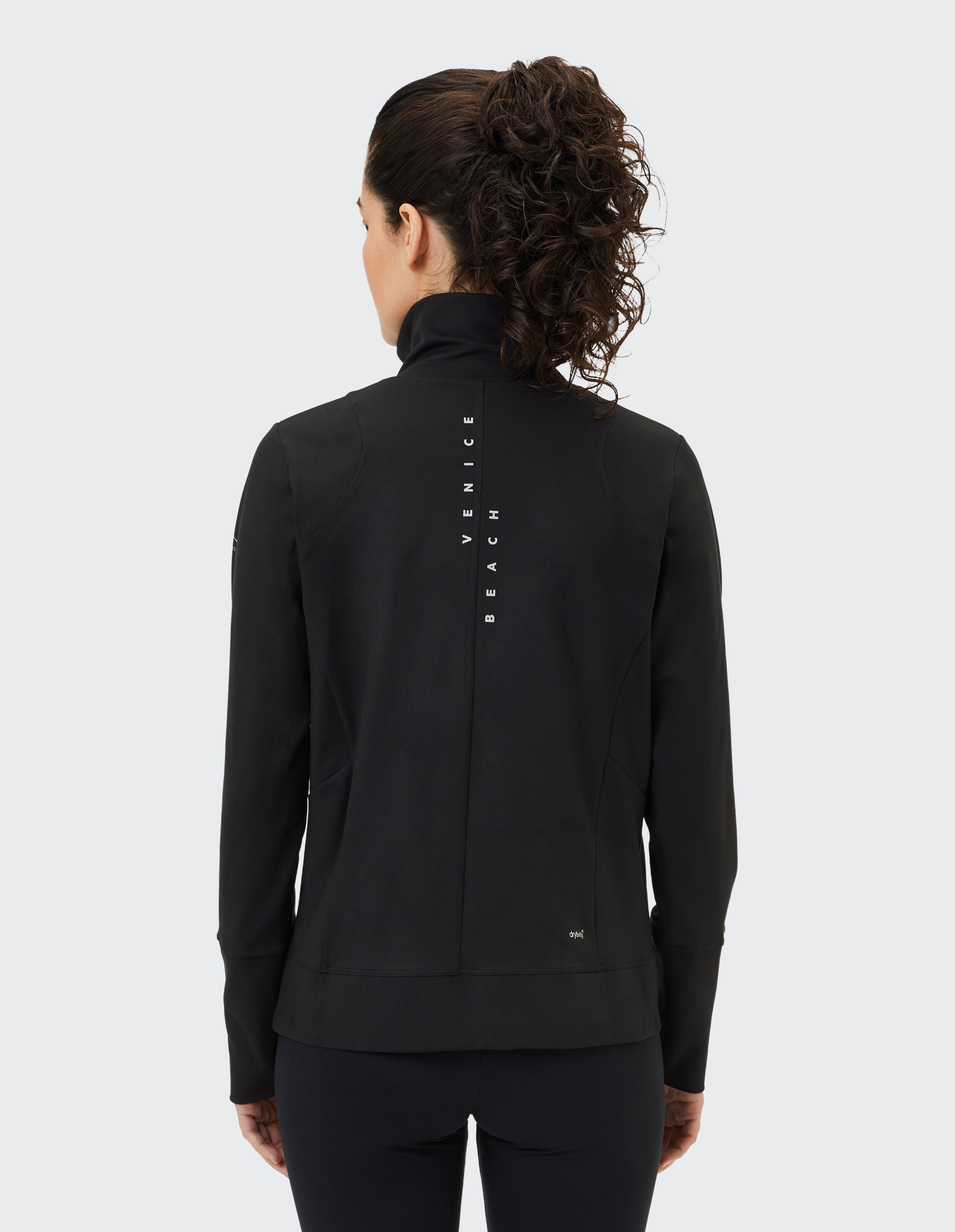Rückansicht einer Frau in einer schwarzen Jacke mit dem Branding von Venice Beach.