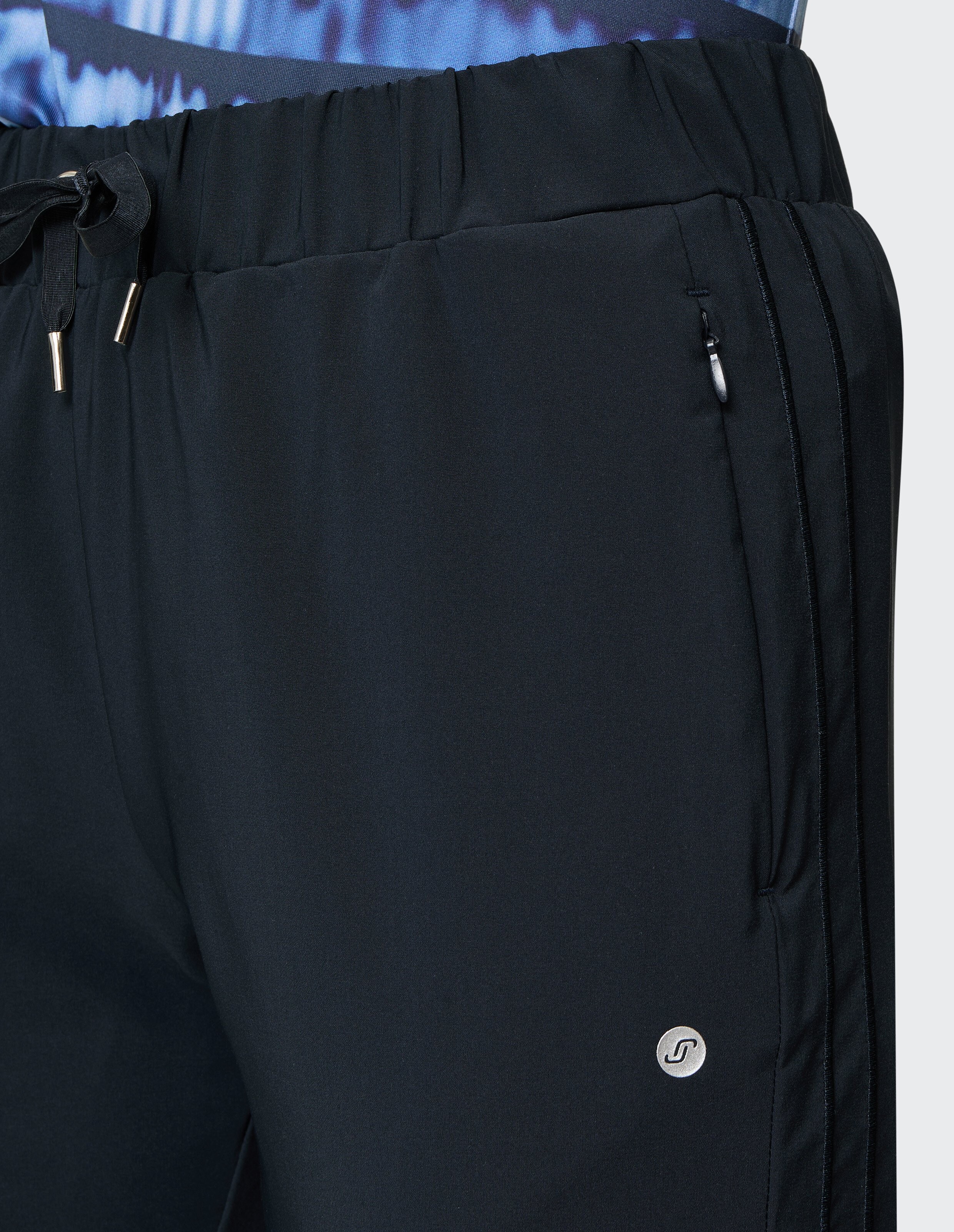 Nahaufnahme einer dunkelblauen Sporthose mit Reißverschlusstasche, elastischem Bund und einem kleinen, runden, silbernen Logo.